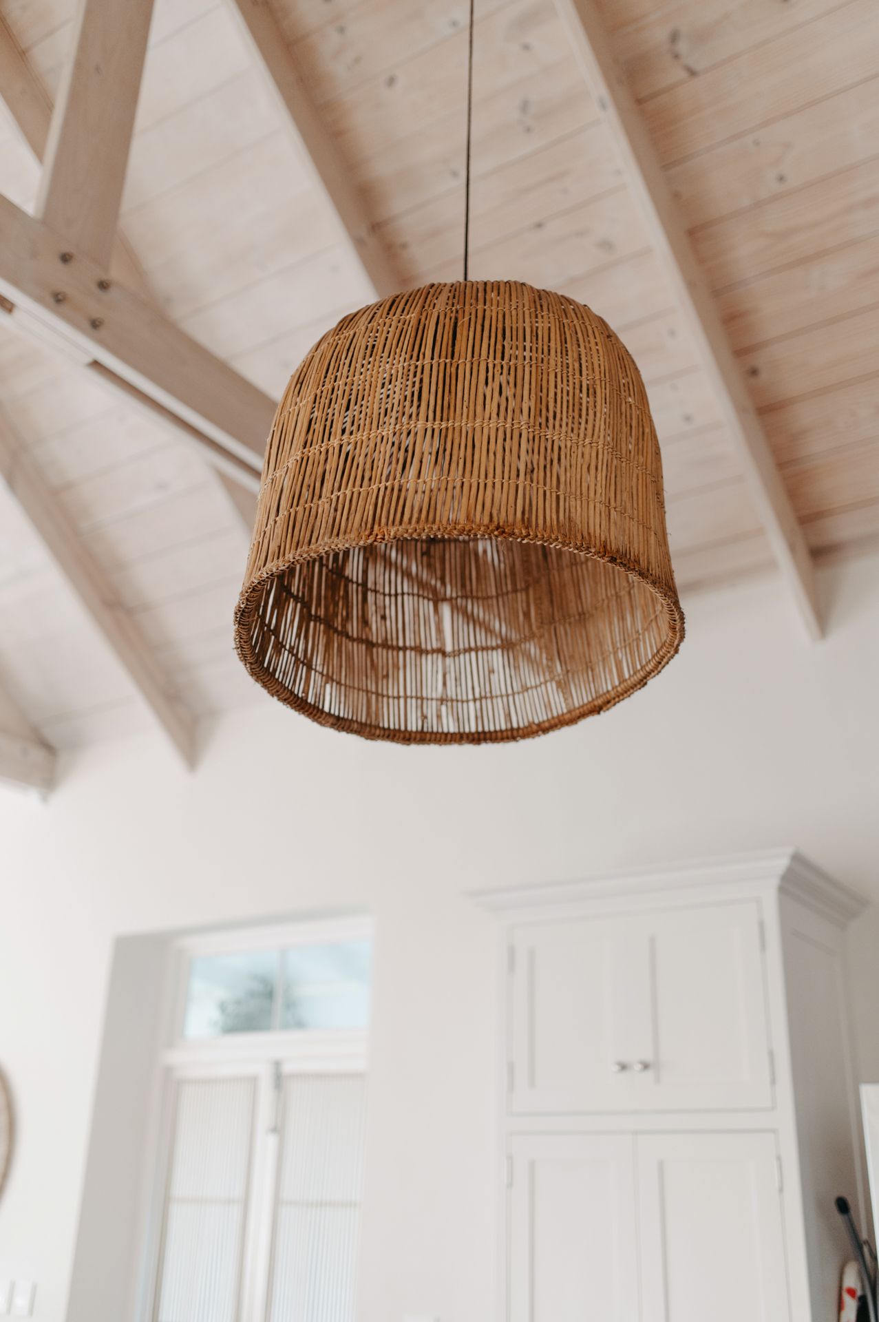 Three woven rattan pendant lights hang from a white vaulted ceiling in a modern coastal-style interior.