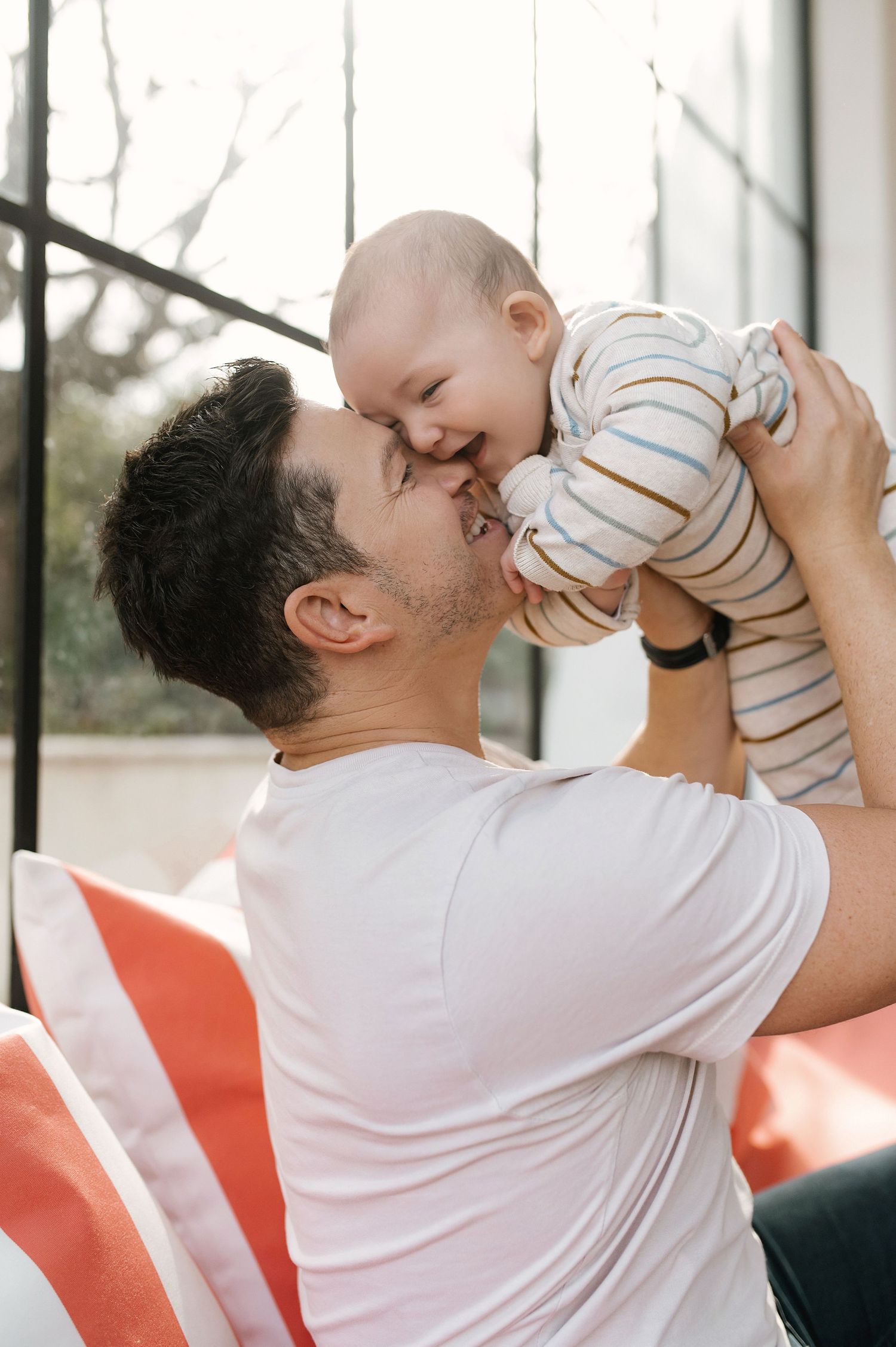A tender moment captured as a baby in striped clothing is lifted up for a playful interaction indoors.