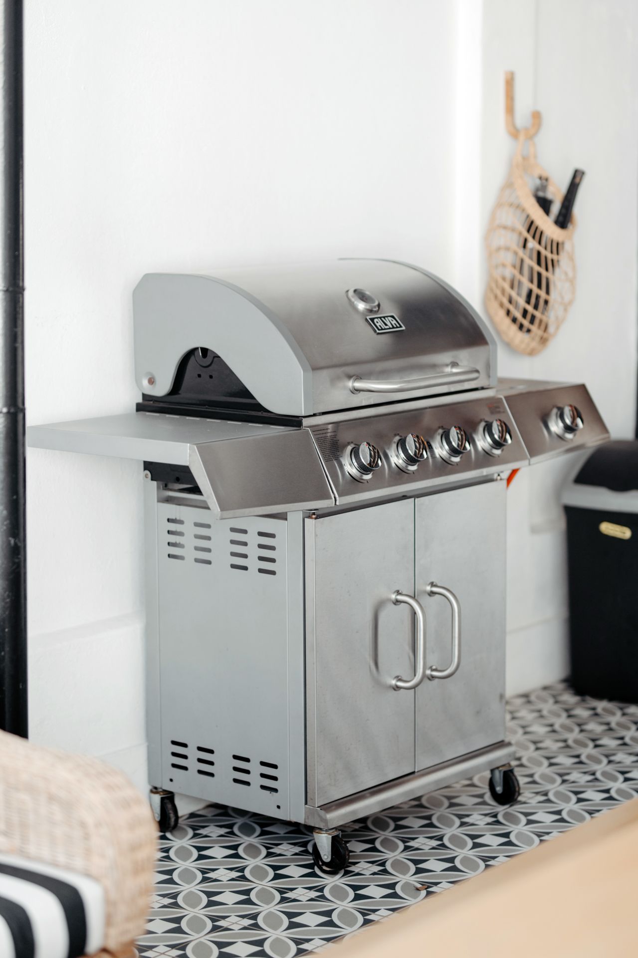 Stainless steel outdoor grill with cabinet base sits on patterned tile floor in modern kitchen setting.