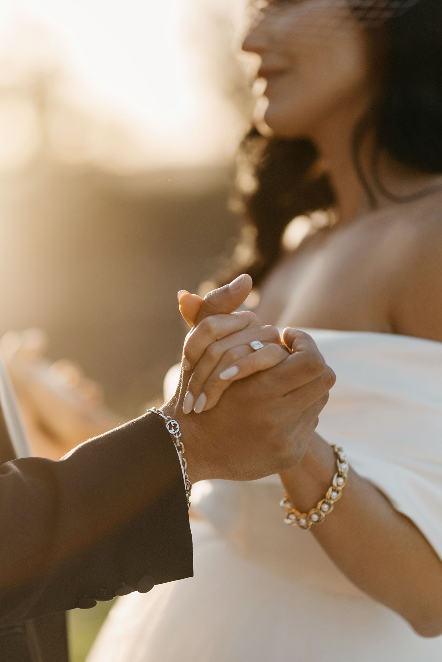 Couple holds hands at sunset wedding ceremony with bride wearing white dress and sparkling bracelet.