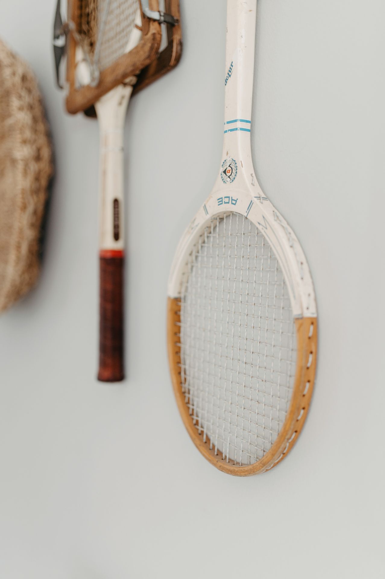 A vintage wooden tennis racket with white and tan coloring mounted on a light gray wall.