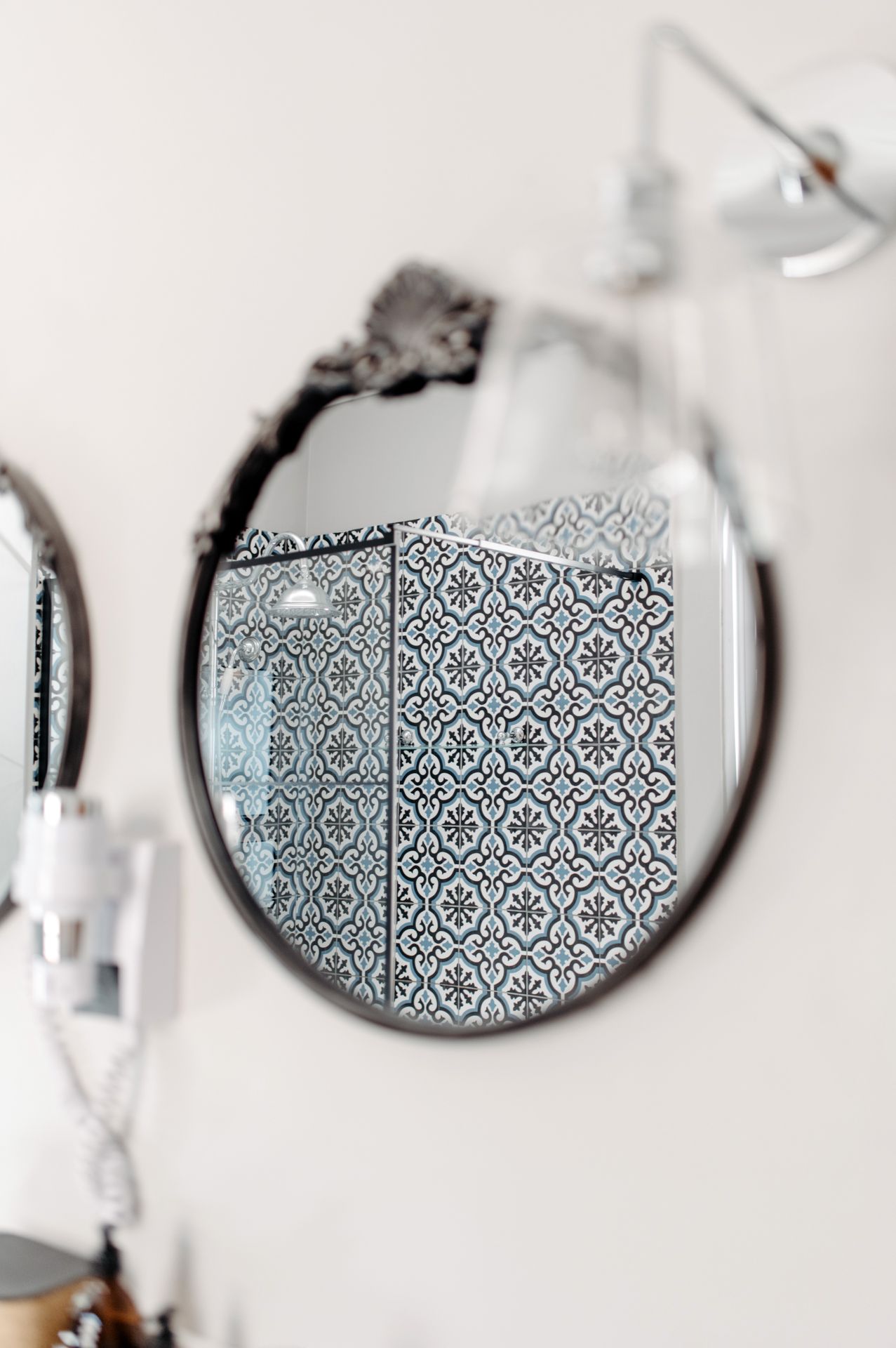 Round mirror on white wall reflects black and white geometric patterned wallpaper in bathroom interior.
