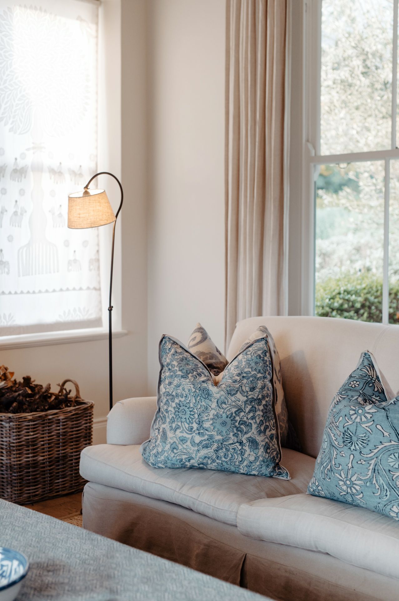 A modern living room sofa with blue and white patterned throw pillows next to large windows with natural light.
