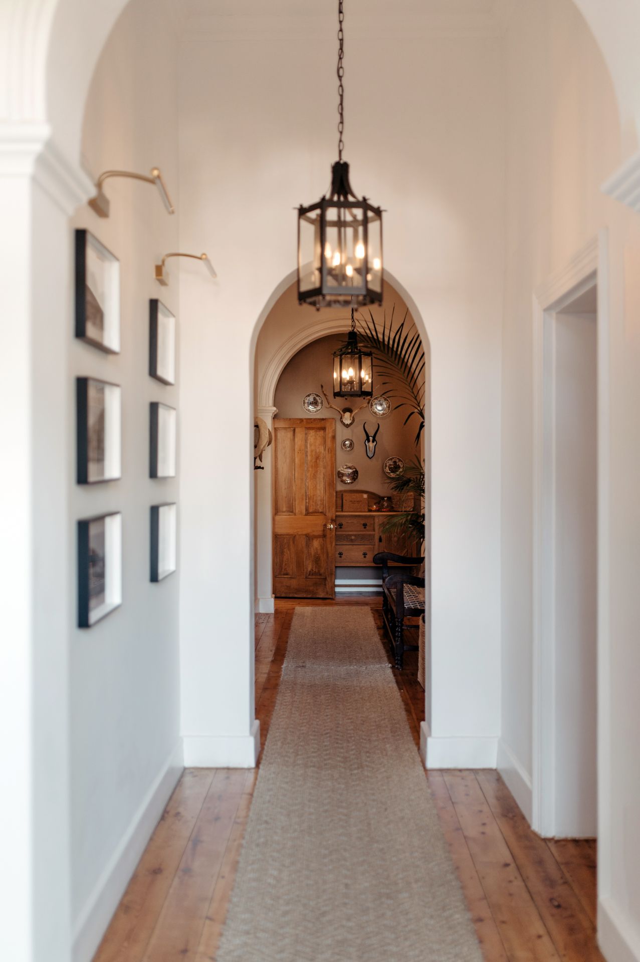 A long white arched hallway with wooden doors and hanging pendant lights creates an elegant corridor perspective.
