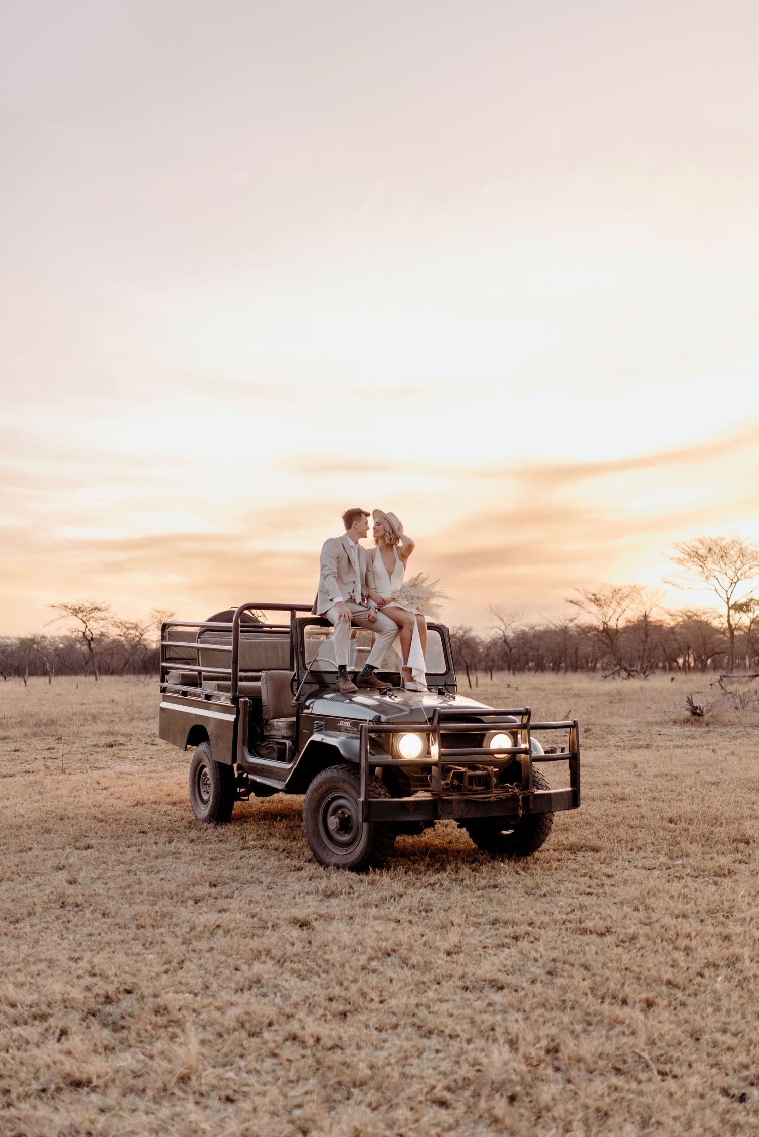 Safari vehicle parked in golden savanna grassland during sunset with couple enjoying romantic moment in Africa.