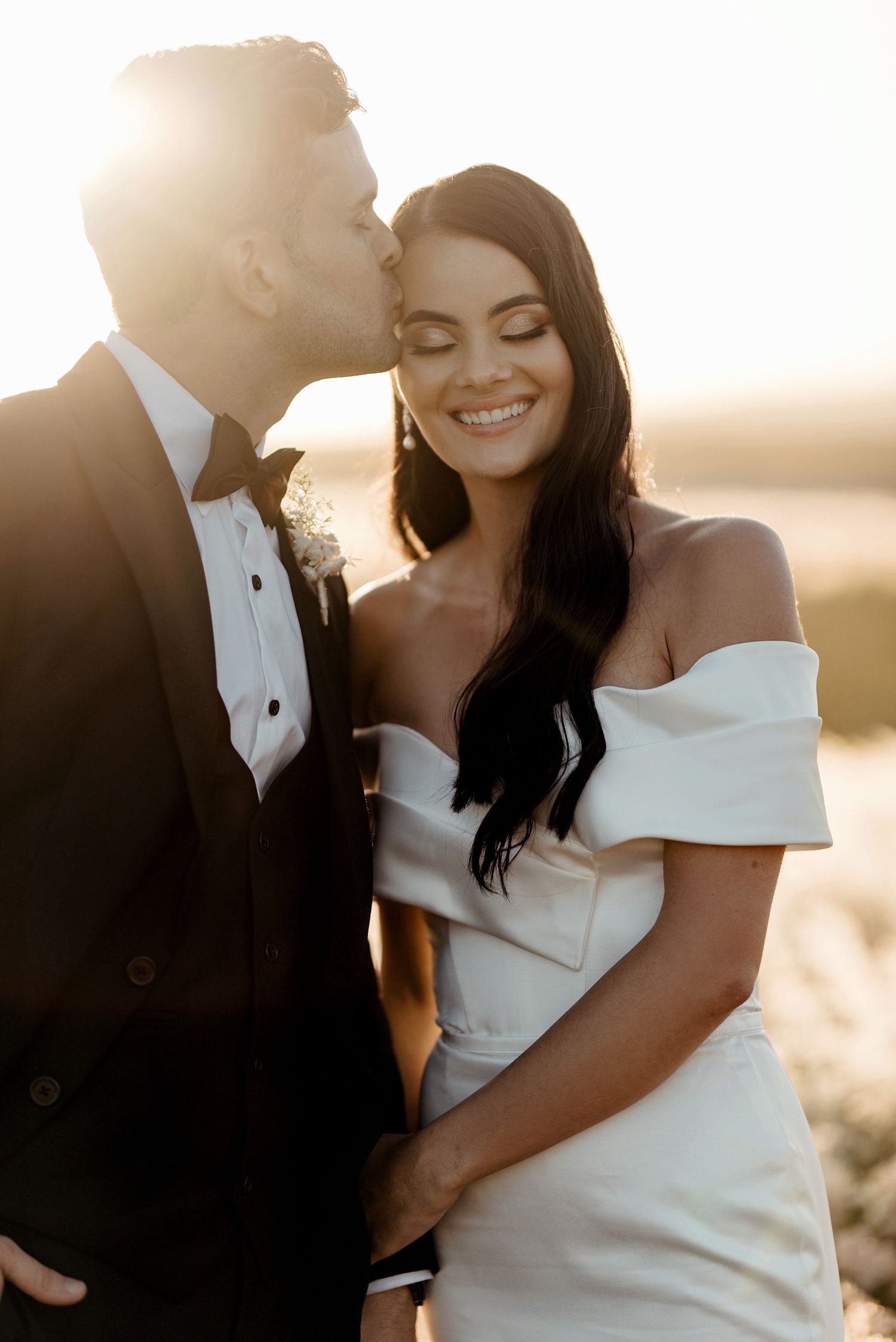 Romantic wedding couple embraces in golden sunlight during sunset photoshoot.