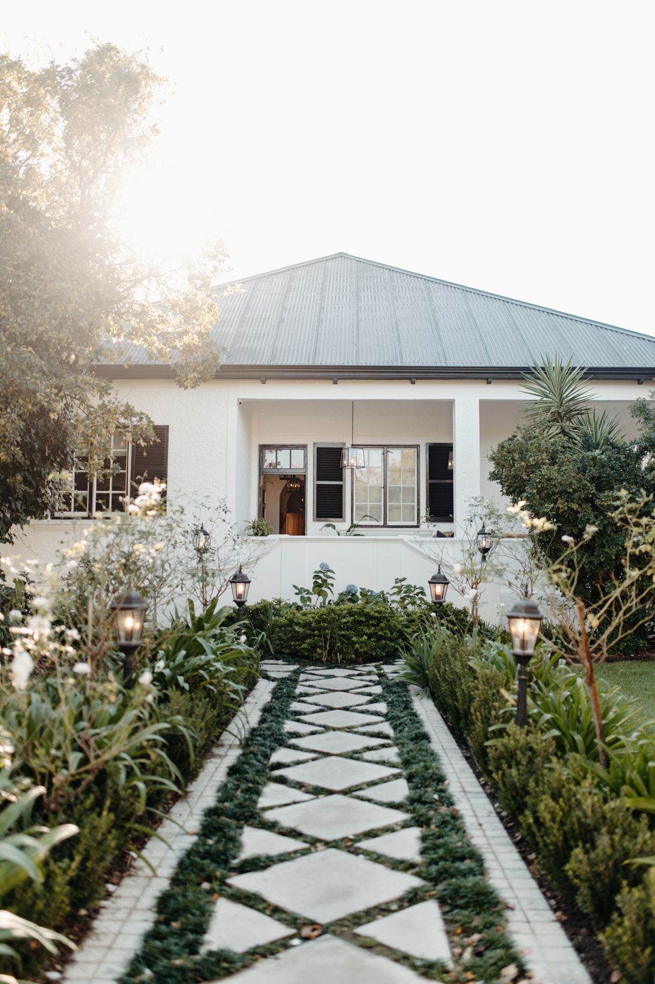 Modern white house with geometric stone pathway through lush garden landscaping and native plants.