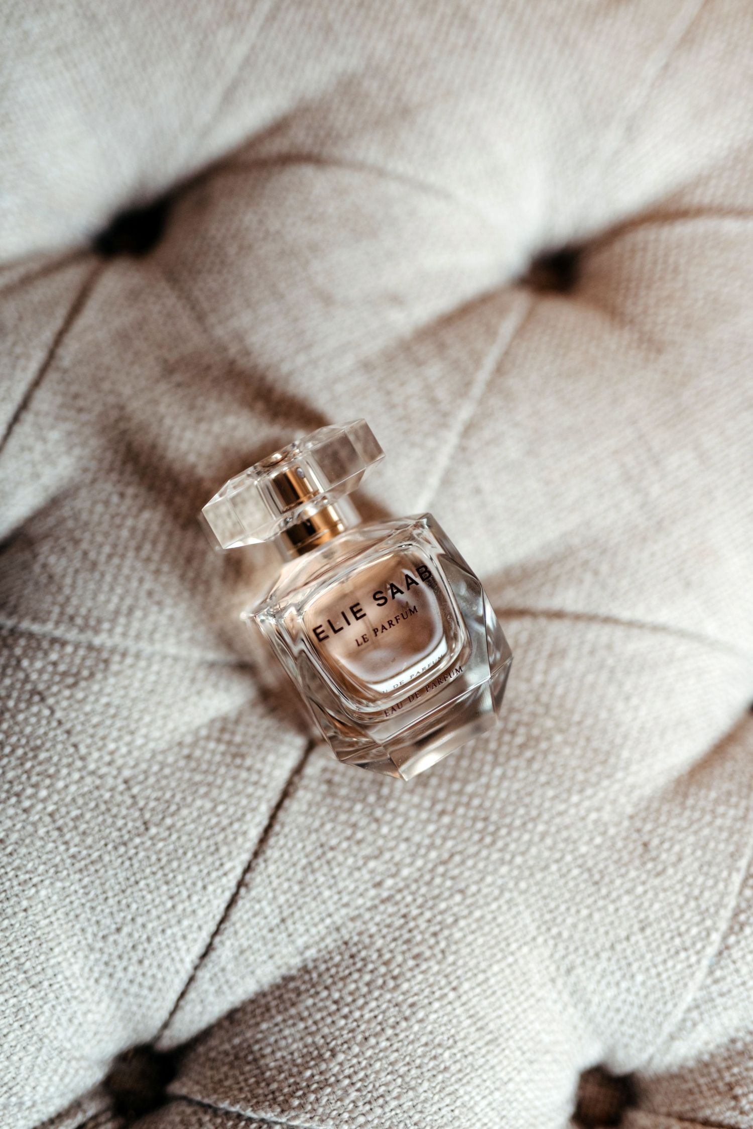 Elegant perfume bottle photographed on textured beige fabric with soft lighting and shallow depth of field.