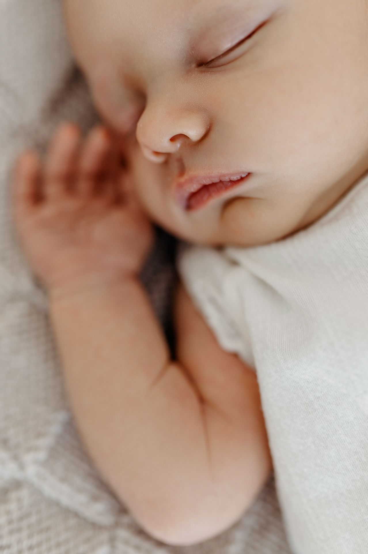 Close-up macro photo showing a peacefully sleeping baby nestled in soft white bedding.