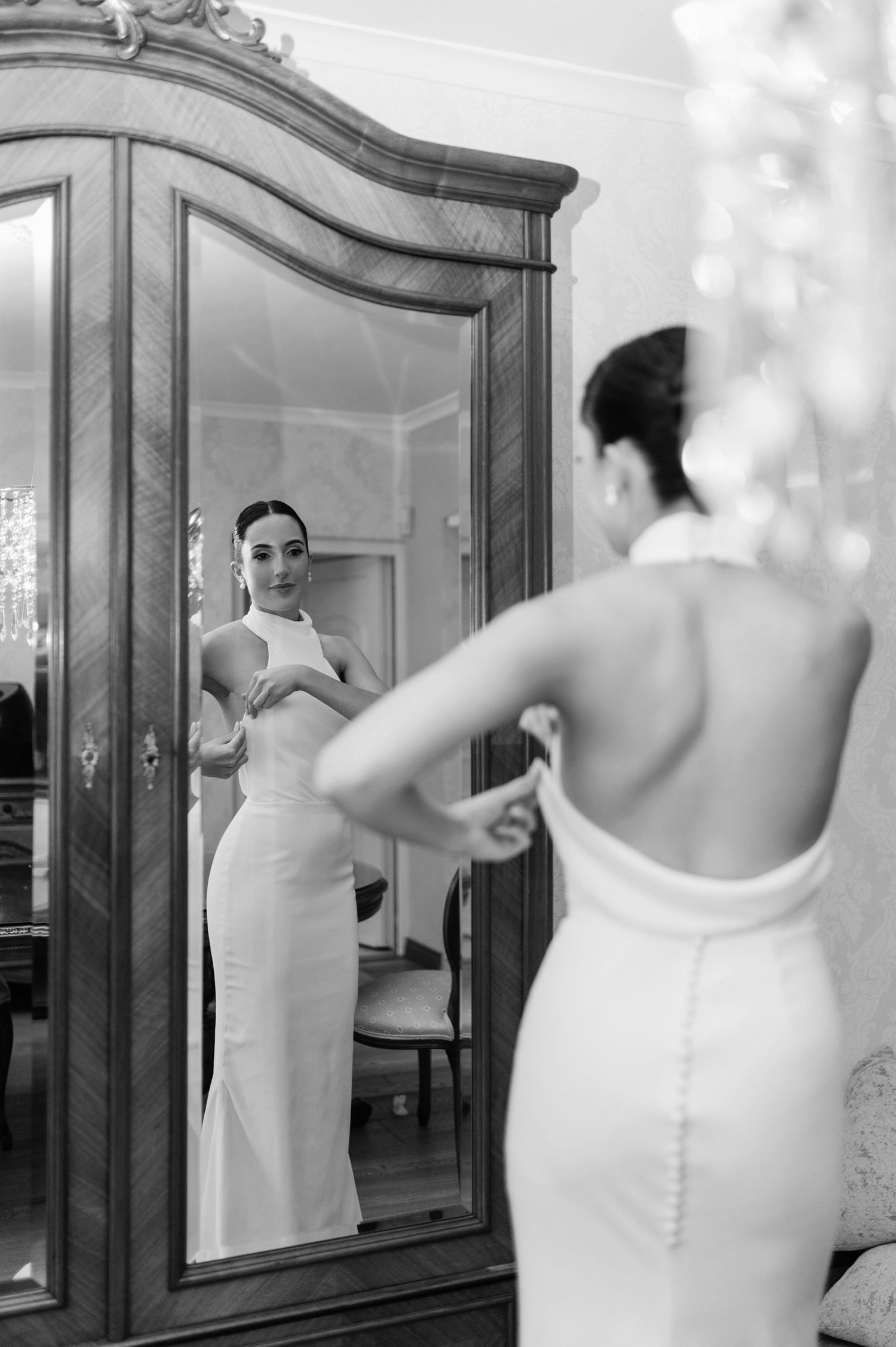 Elegant bride in fitted dress looking at reflection in vintage mirror.