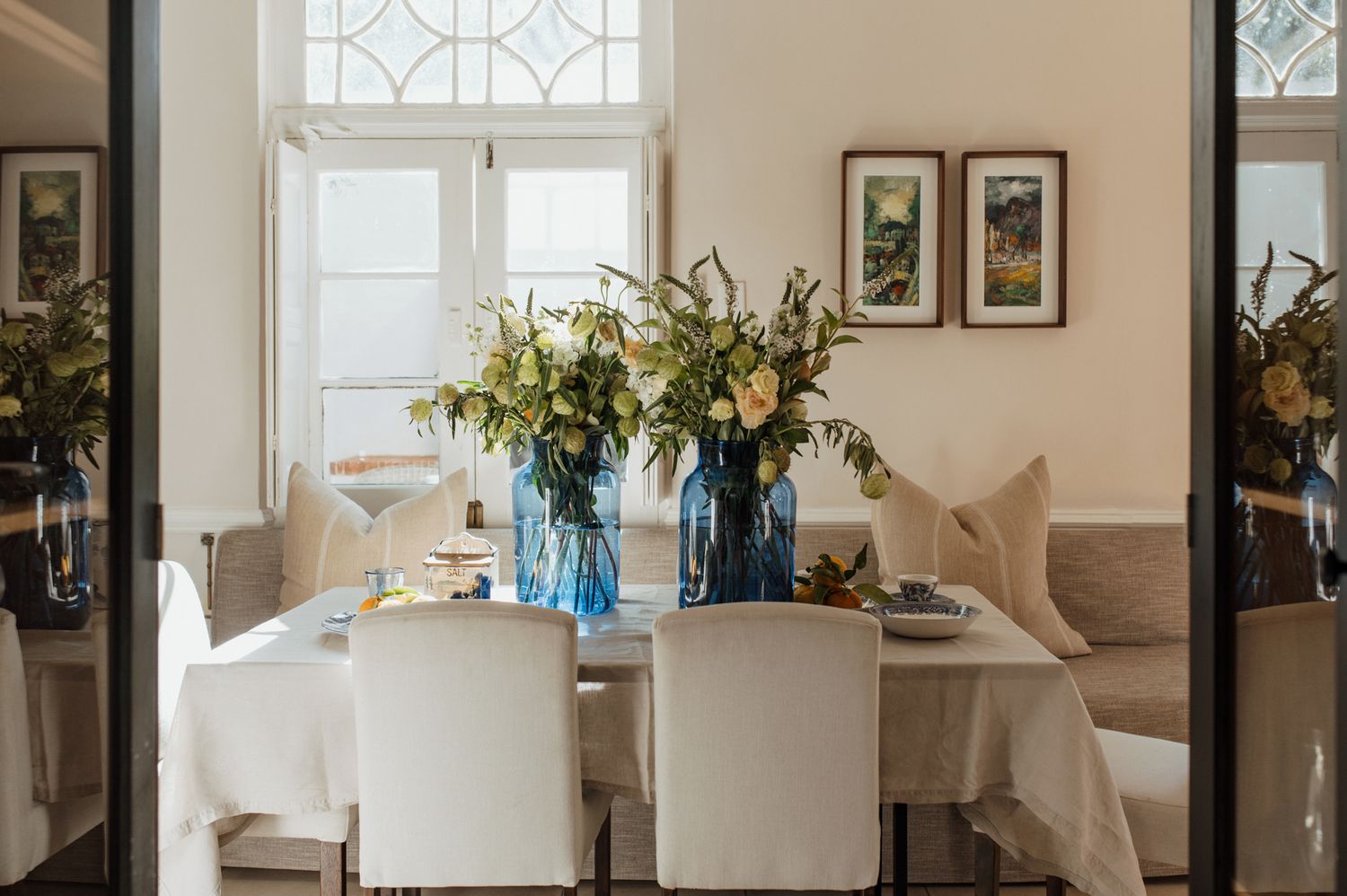 A bright and airy living room features decorative transom windows, blue glass vases, and white walls with framed artwork.