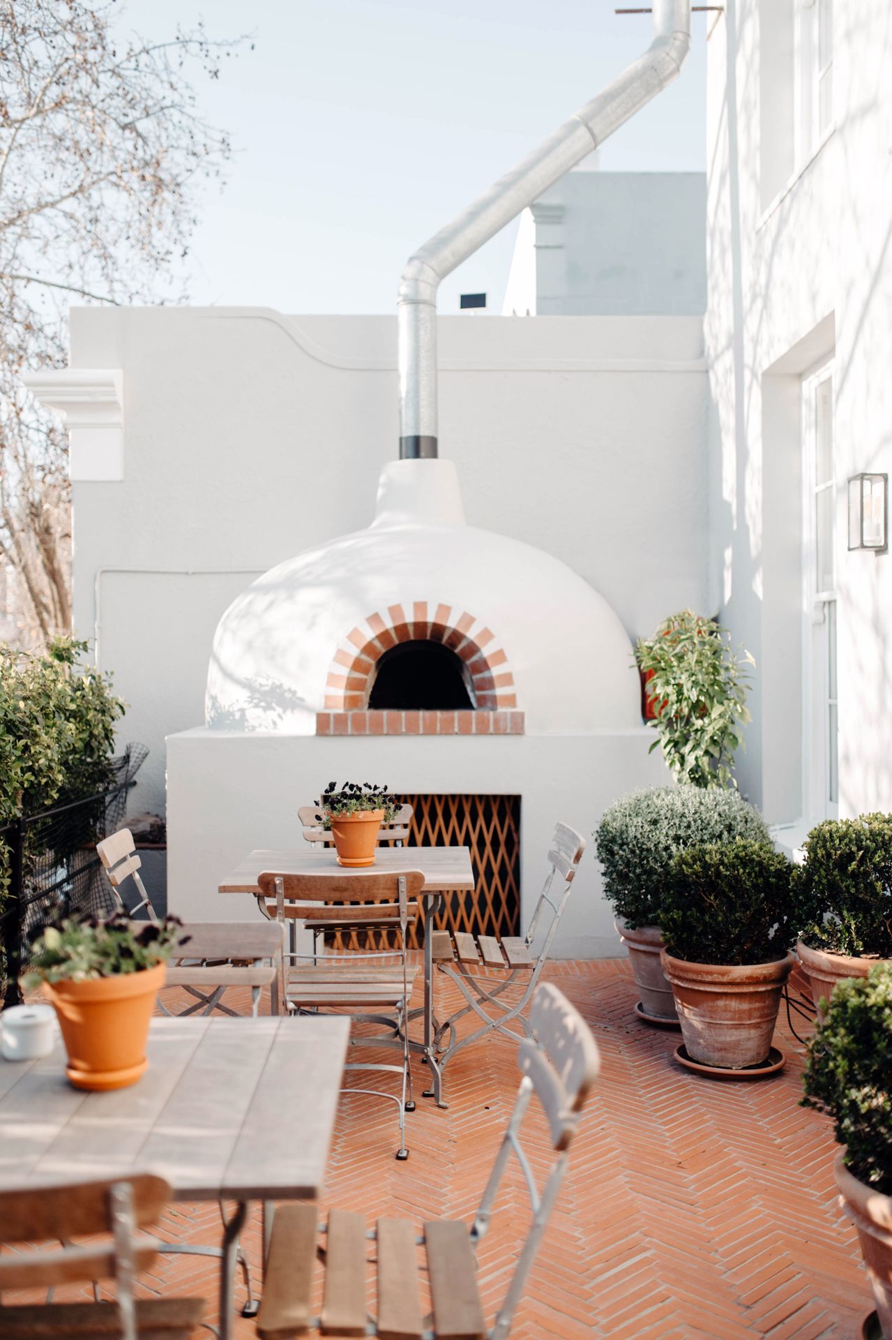 Mediterranean terrace with herringbone brick flooring, white walls, and terracotta planters creates a cozy outdoor living space.