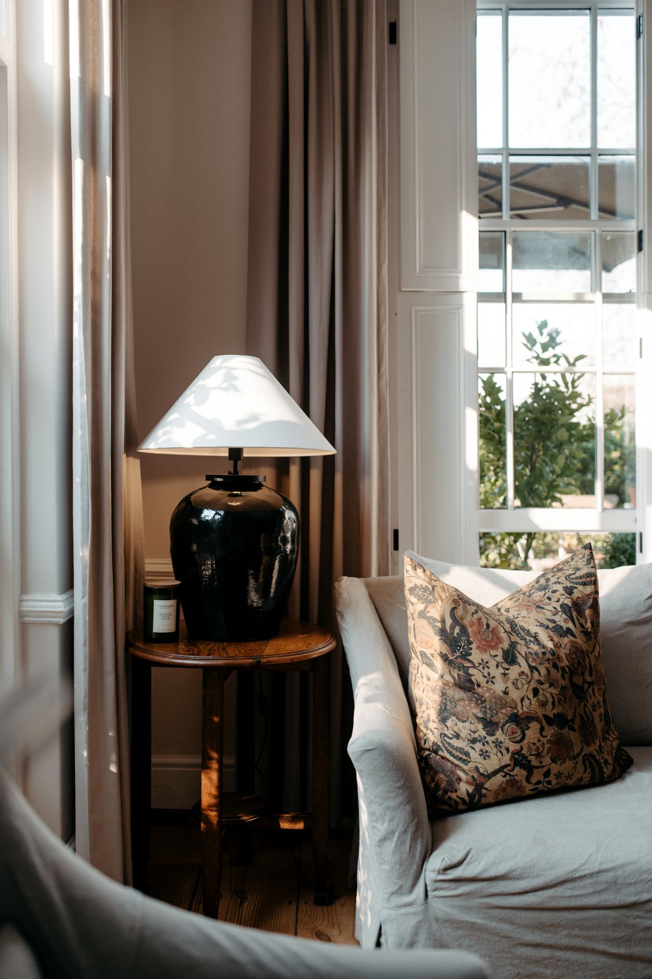 Elegant living room interior with tall windows, white curtains, and cozy seating area featuring decorative throw pillows.