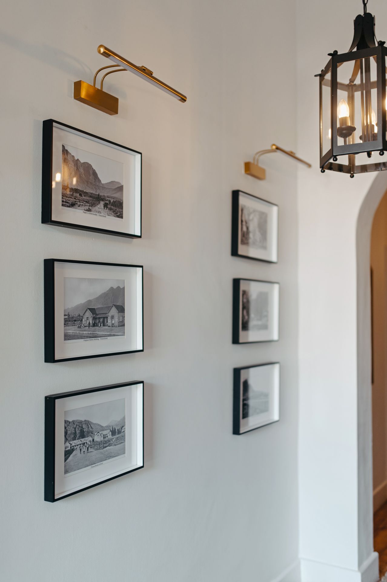 A gallery wall displays black and white framed photographs along a white hallway with modern brass light fixtures.