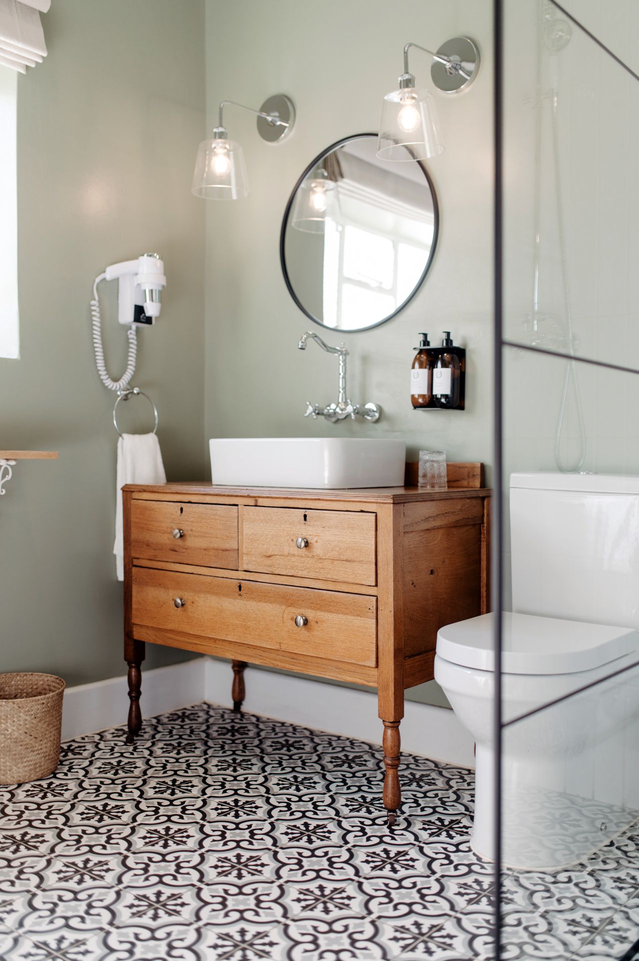 Modern bathroom with wooden vanity and striking black and white geometric floor tiles beneath circular mirror.
