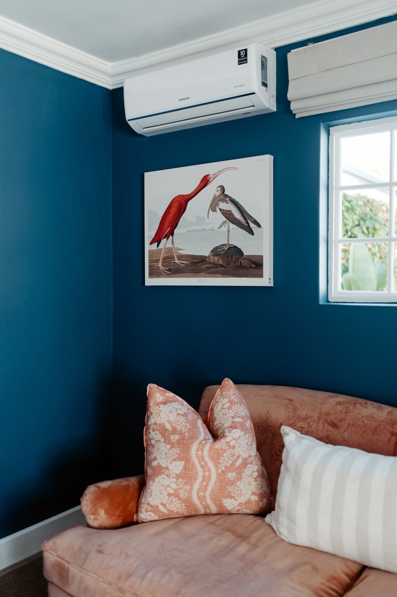 Modern bedroom with deep teal walls, white trim, and coral accents features minimalist bird artwork and a wall-mounted AC unit.