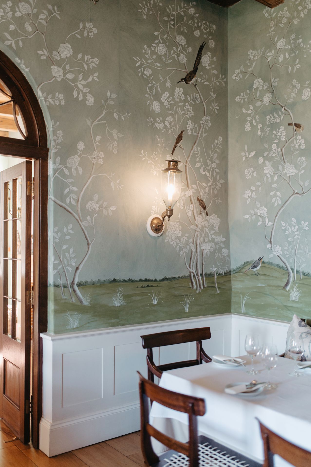 Elegant dining room with hand-painted chinoiserie wallpaper featuring delicate floral patterns and arched doorways.