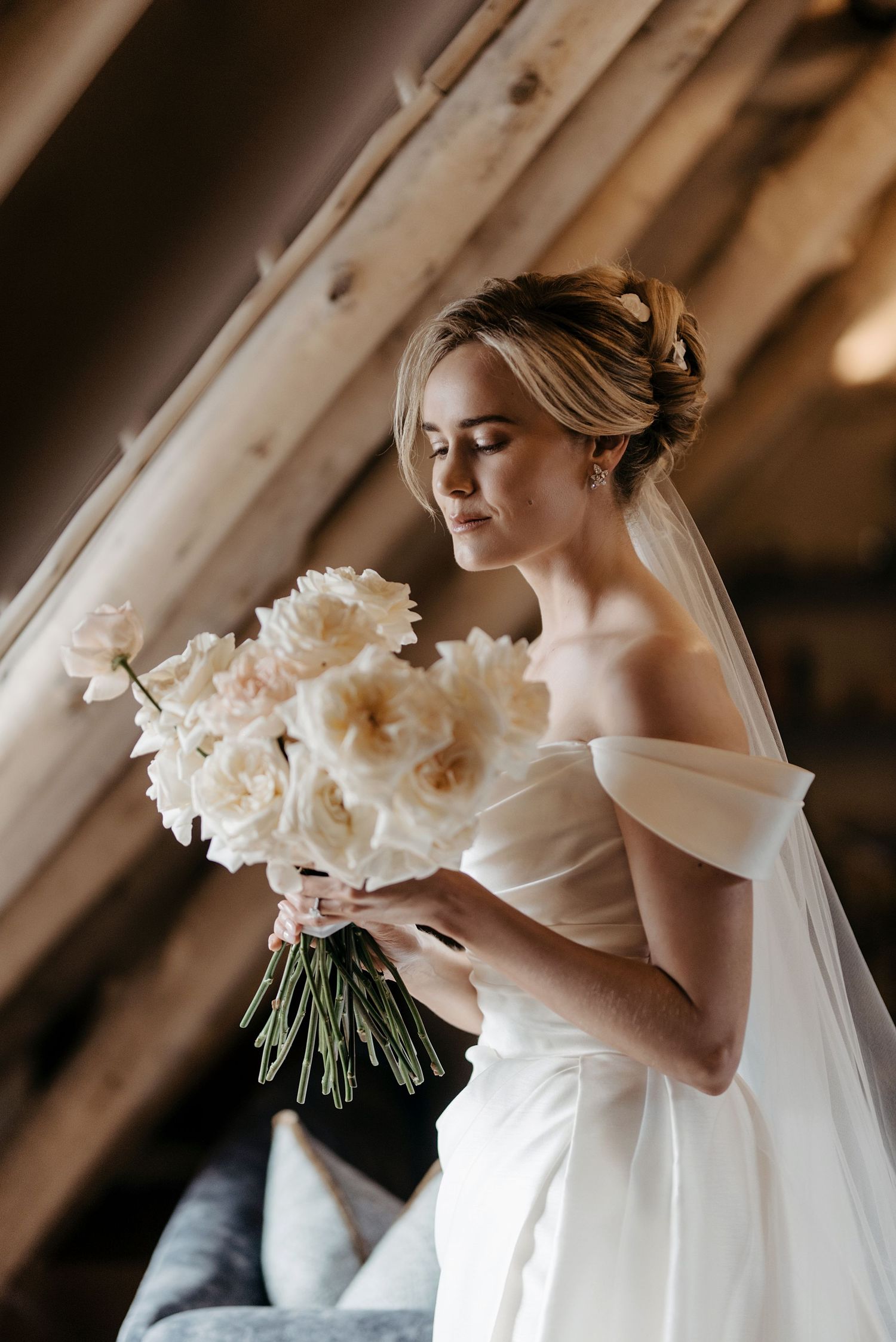 A bride in a white wedding gown holds a classic bouquet of white flowers against a soft, warm background.