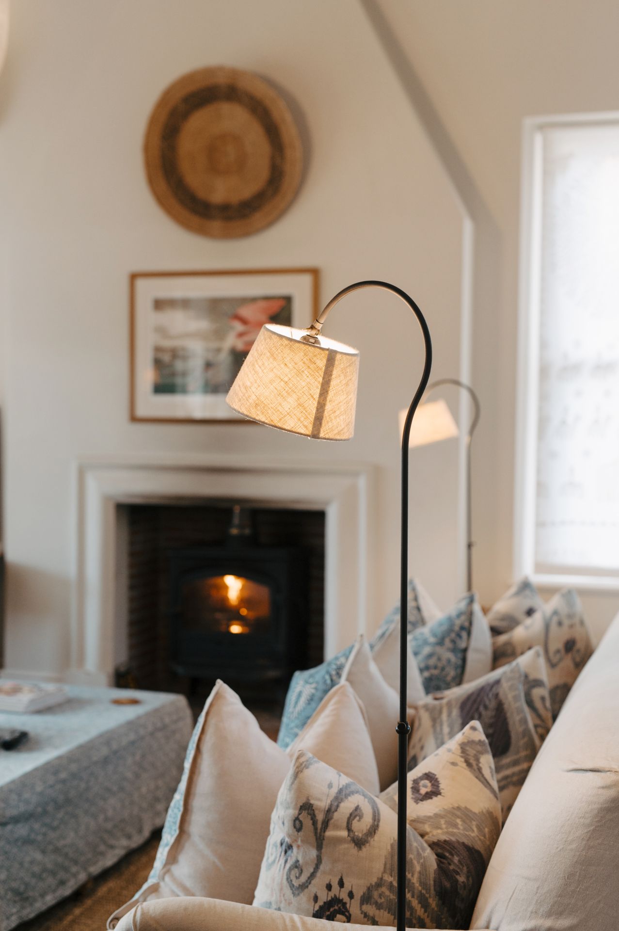 A cozy living room interior with white walls, decorative baskets, throw pillows and arched floor lamps creating warm ambiance.