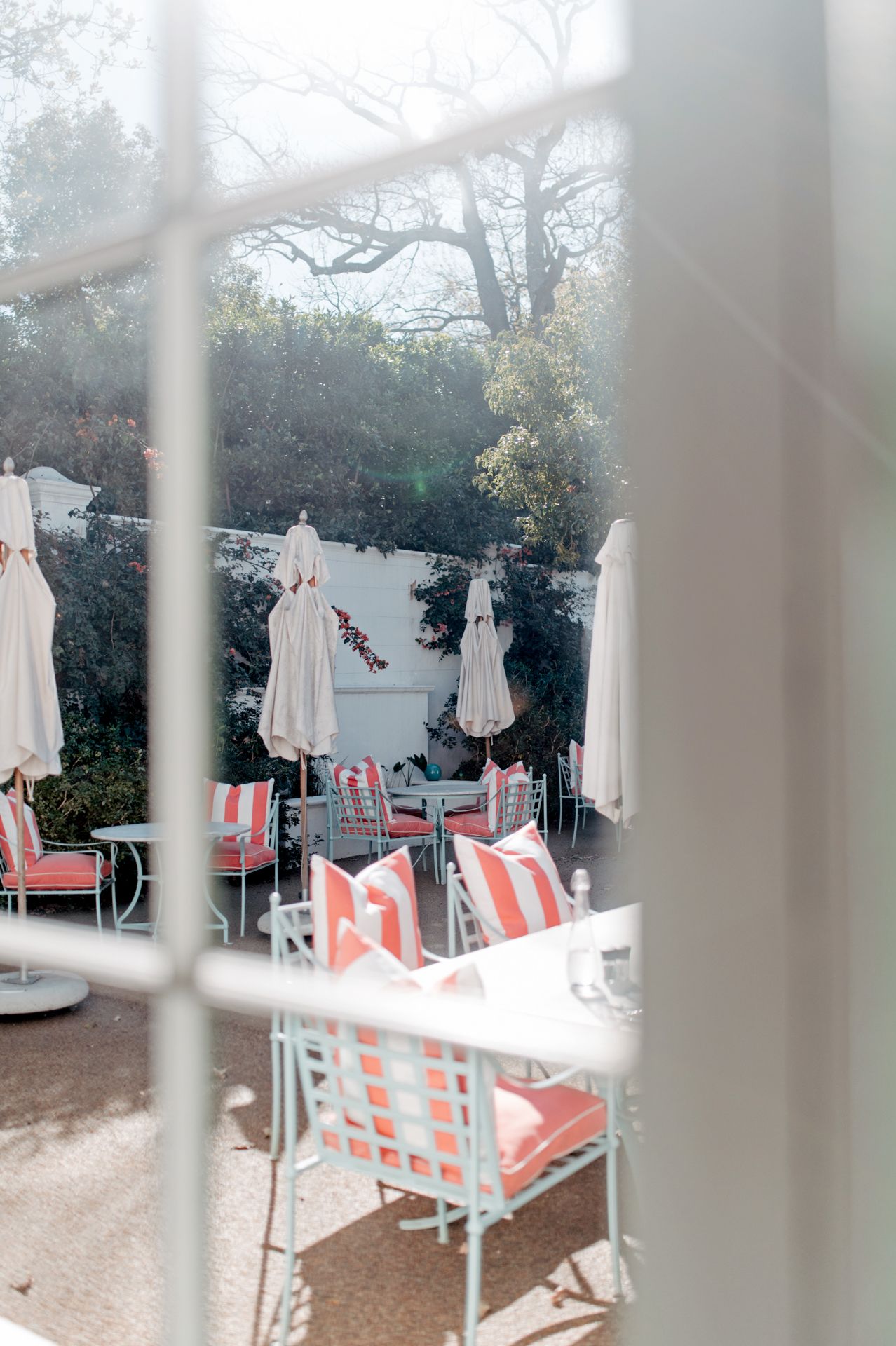 White patio chairs and umbrellas arranged on a terrace viewed through window panes on a misty day.
