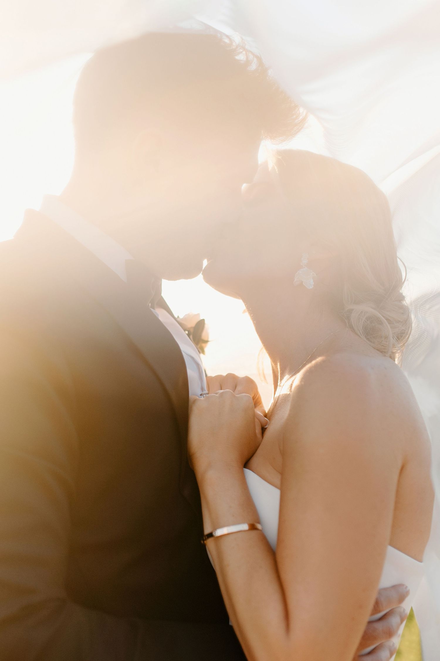 Romantic backlit portrait of couple embracing during wedding ceremony.