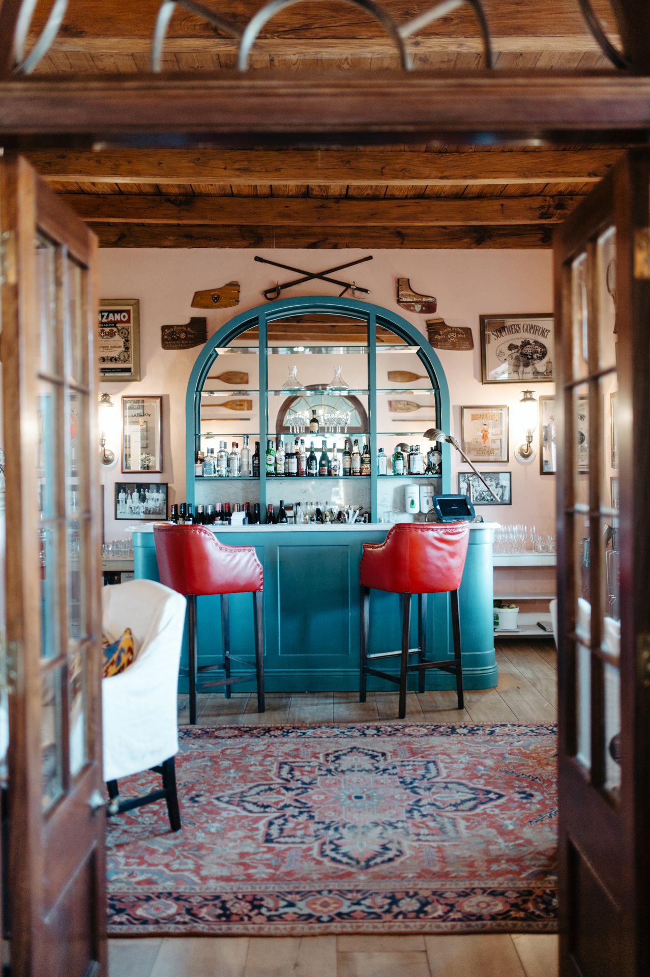 Panoramic view of a rustic bar interior with turquoise accents, red chairs and oriental rugs on hardwood floors.