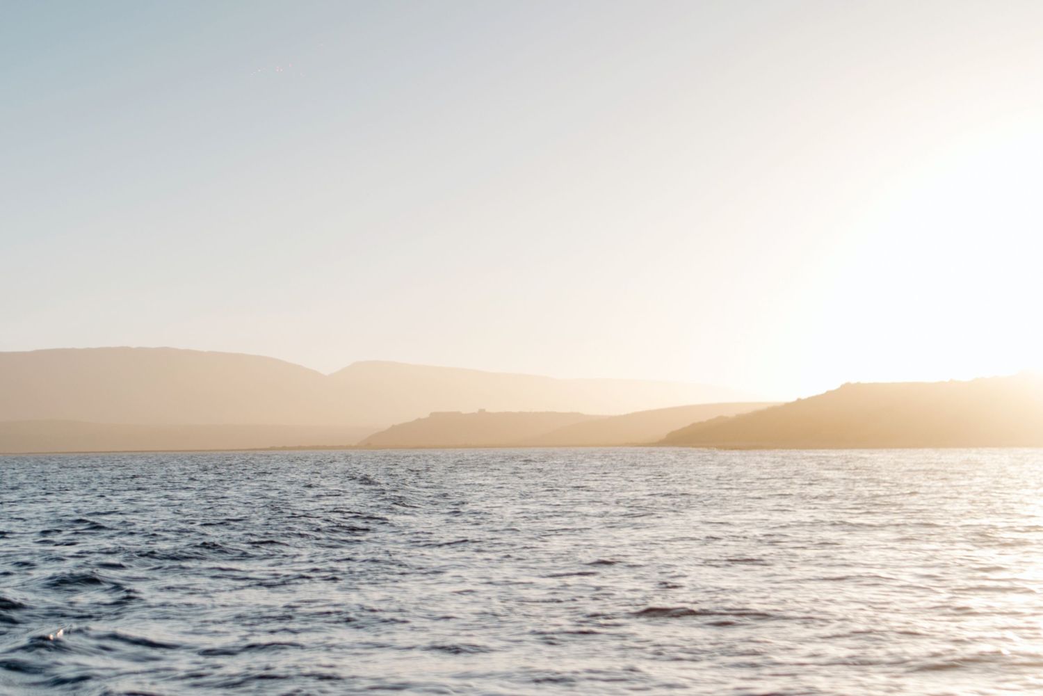 A panoramic seascape features tranquil ocean waves and distant mountains bathed in golden sunset light.