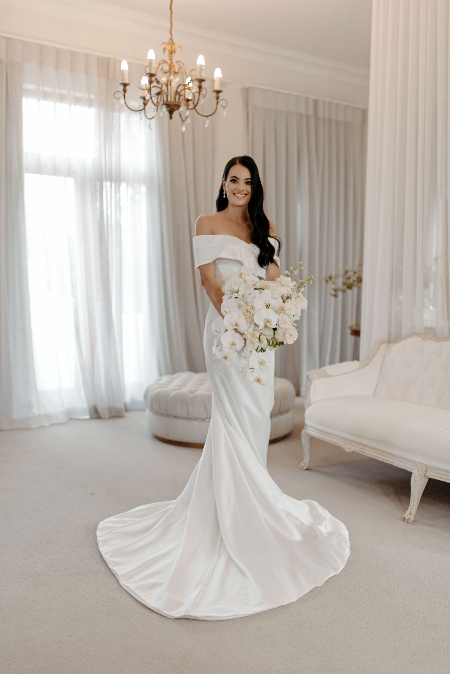 Elegant white bridal portraits in a bright studio with flowing wedding dress and chandelier lighting.