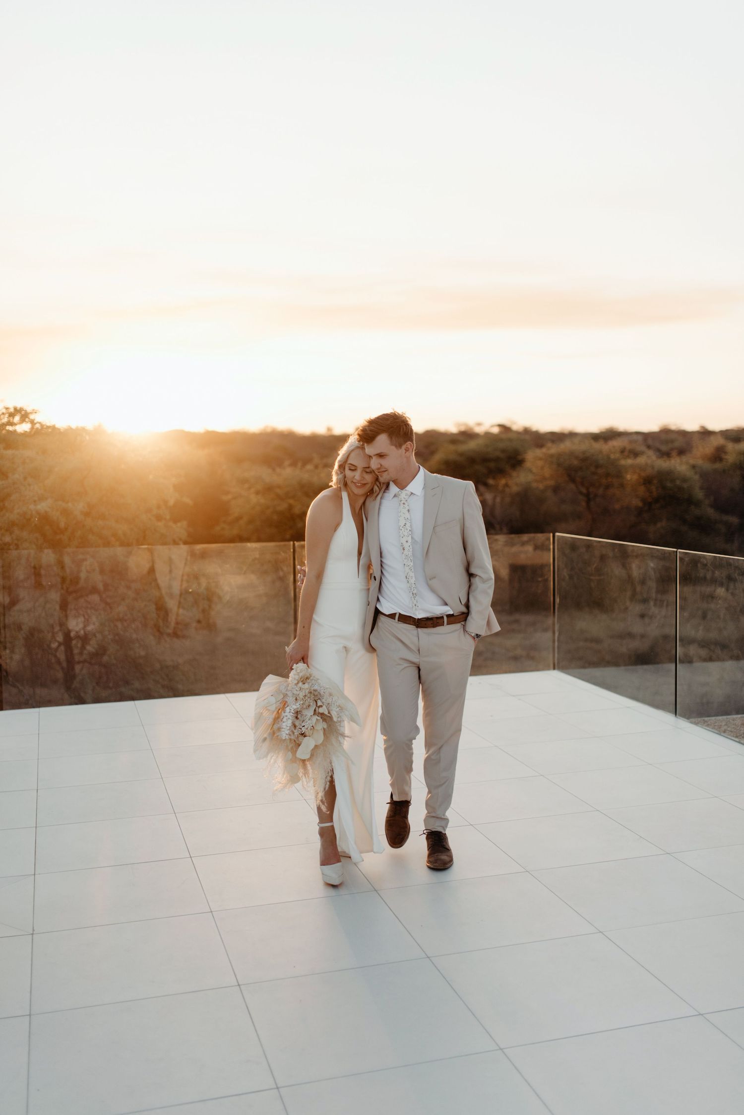 A couple walks together on a white tiled rooftop terrace during golden hour sunset.