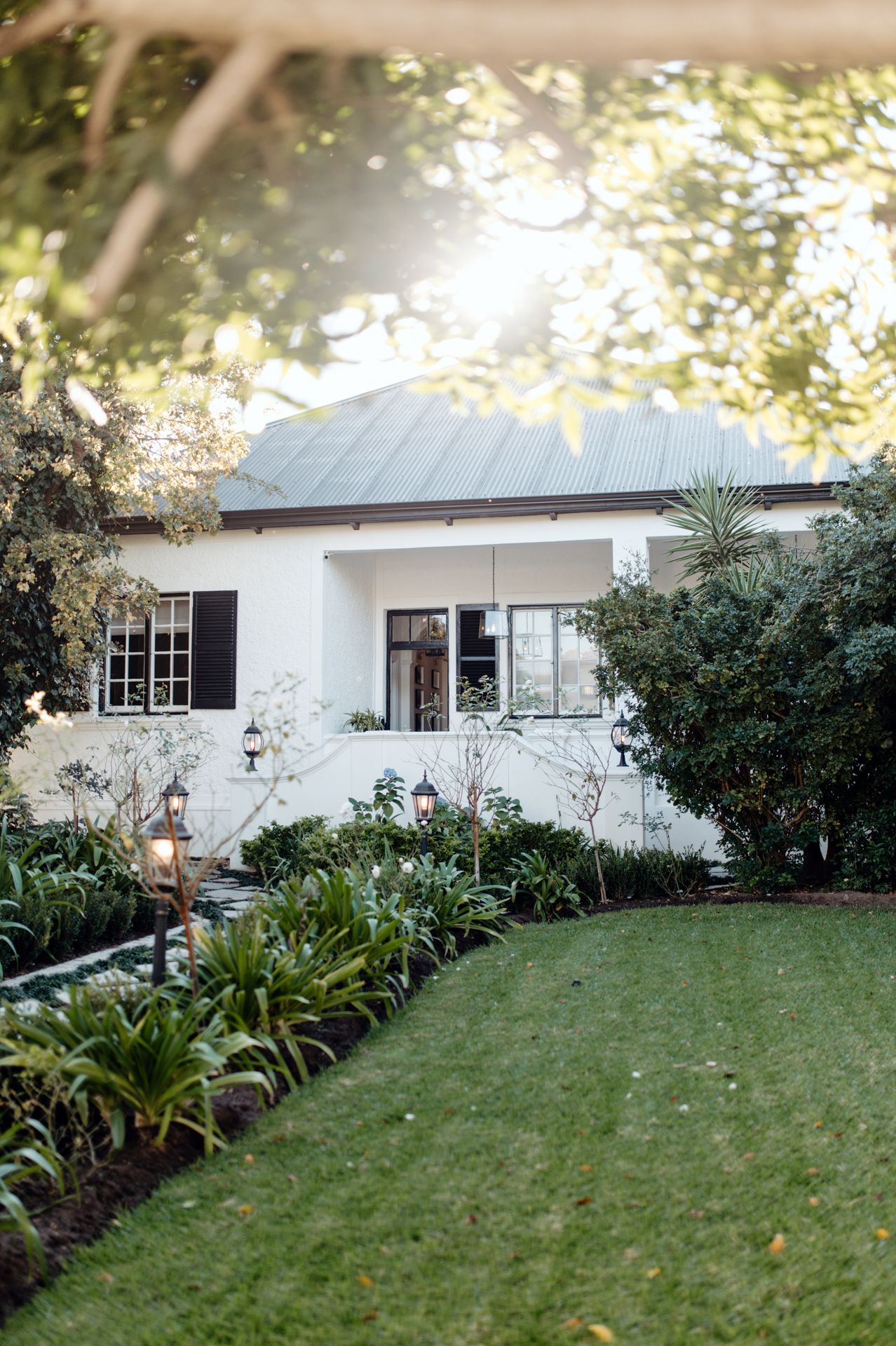White ranch-style house with lush landscaping and green lawn viewed from multiple angles in natural daylight.
