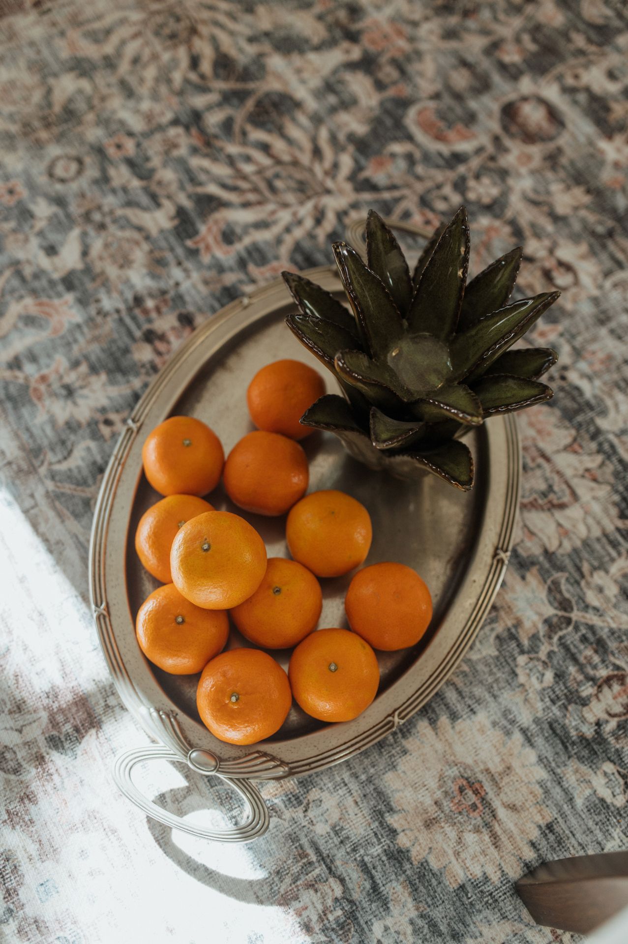 A sequence of photos showing tangerines and a pineapple top arranged on a decorative silver plate against a marble surface.