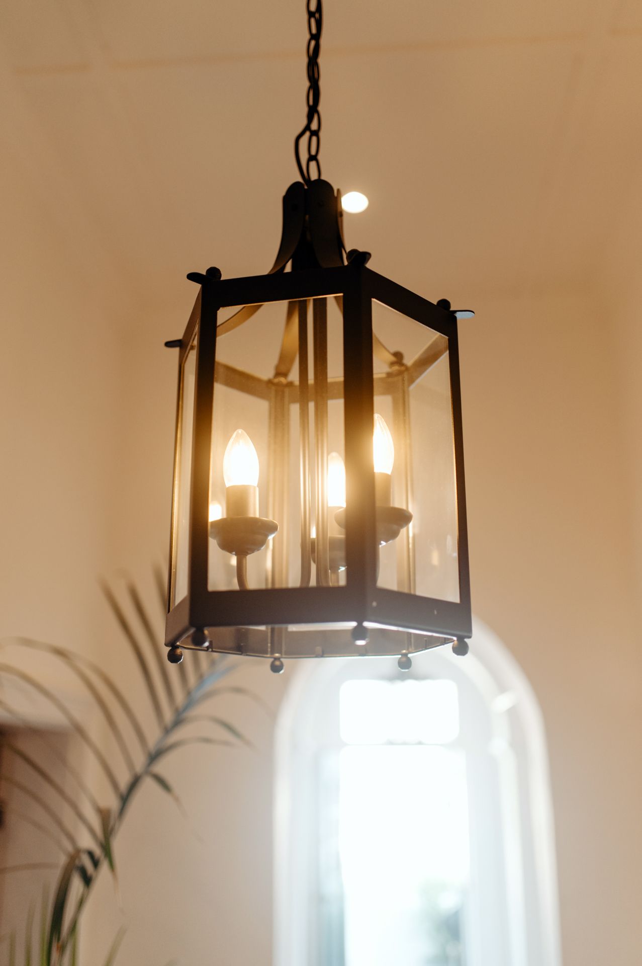 Modern black lantern pendant light fixture with glass panels illuminated against a neutral wall.
