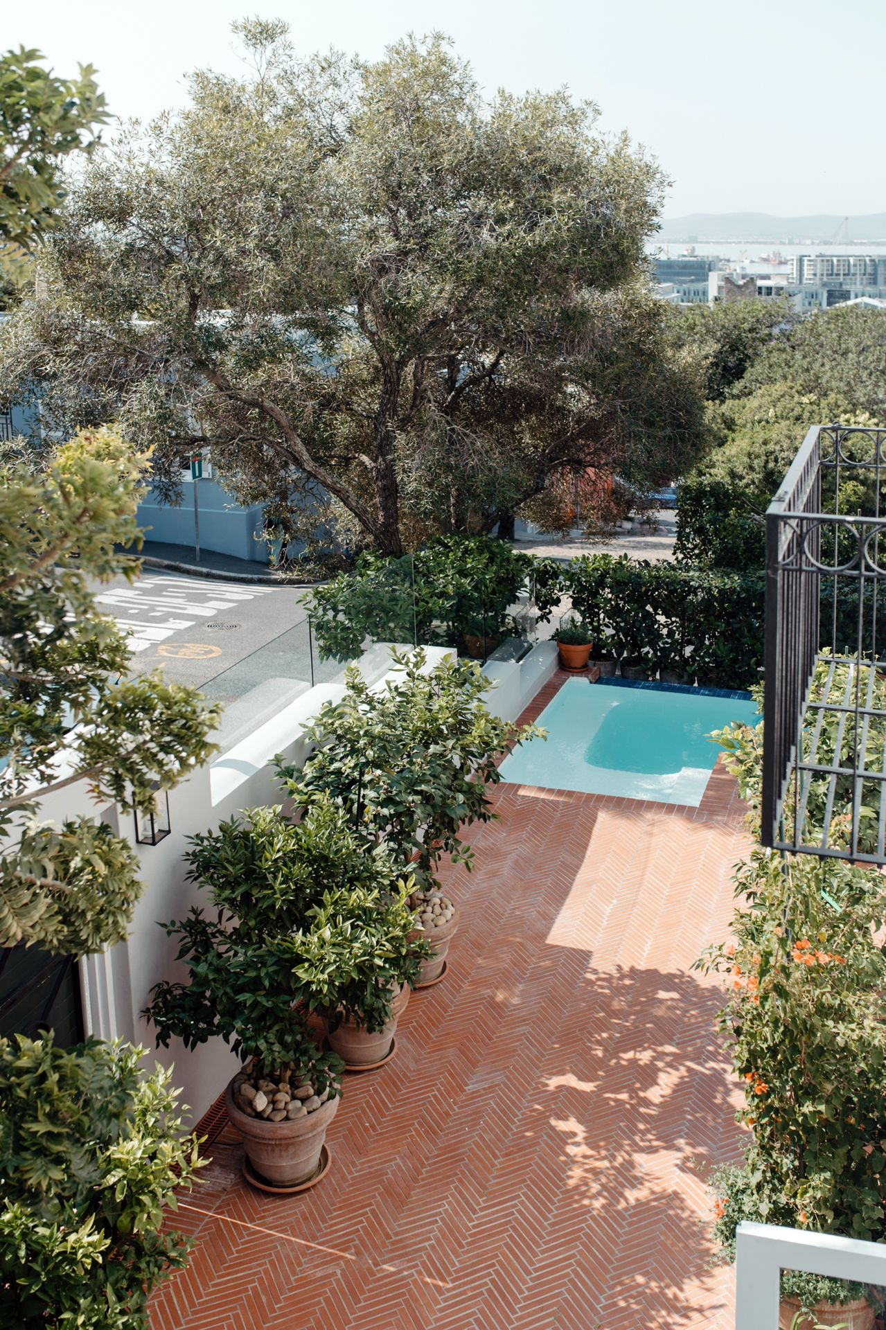 Aerial view of a rooftop terrace with terracotta tiles, potted plants, and a swimming pool in the distance.
