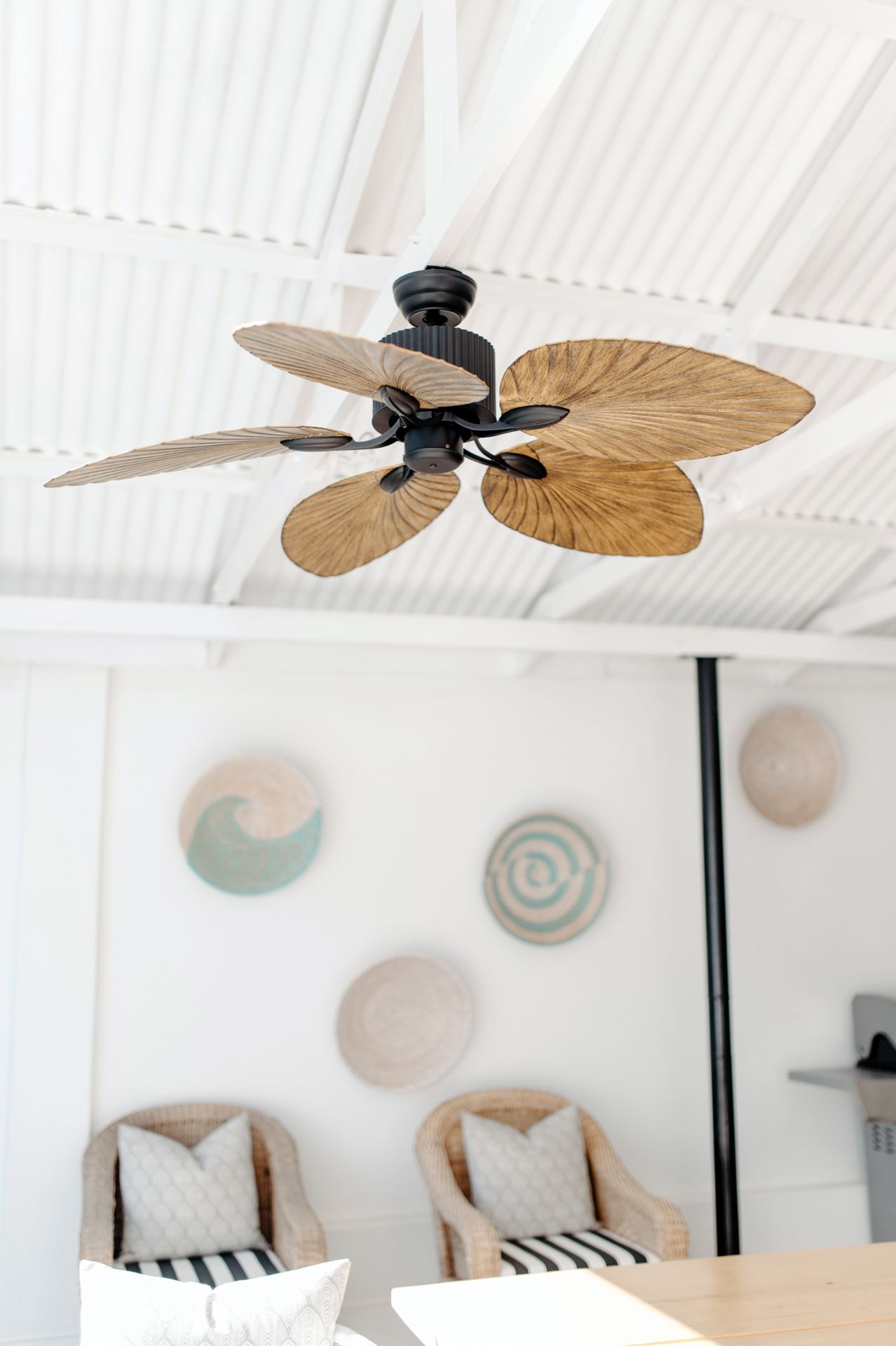 Tropical-style ceiling fan with palm leaf shaped blades mounted on a white ceiling with decorative wall plates.