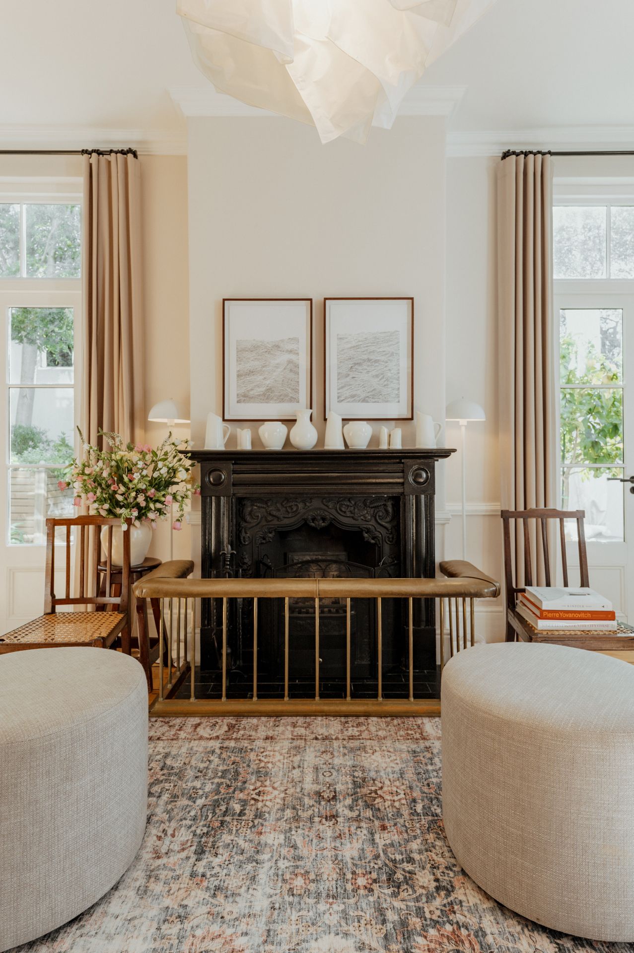 Modern living room with beige curved sofa, patterned area rug, black fireplace mantel and floor-to-ceiling windows.