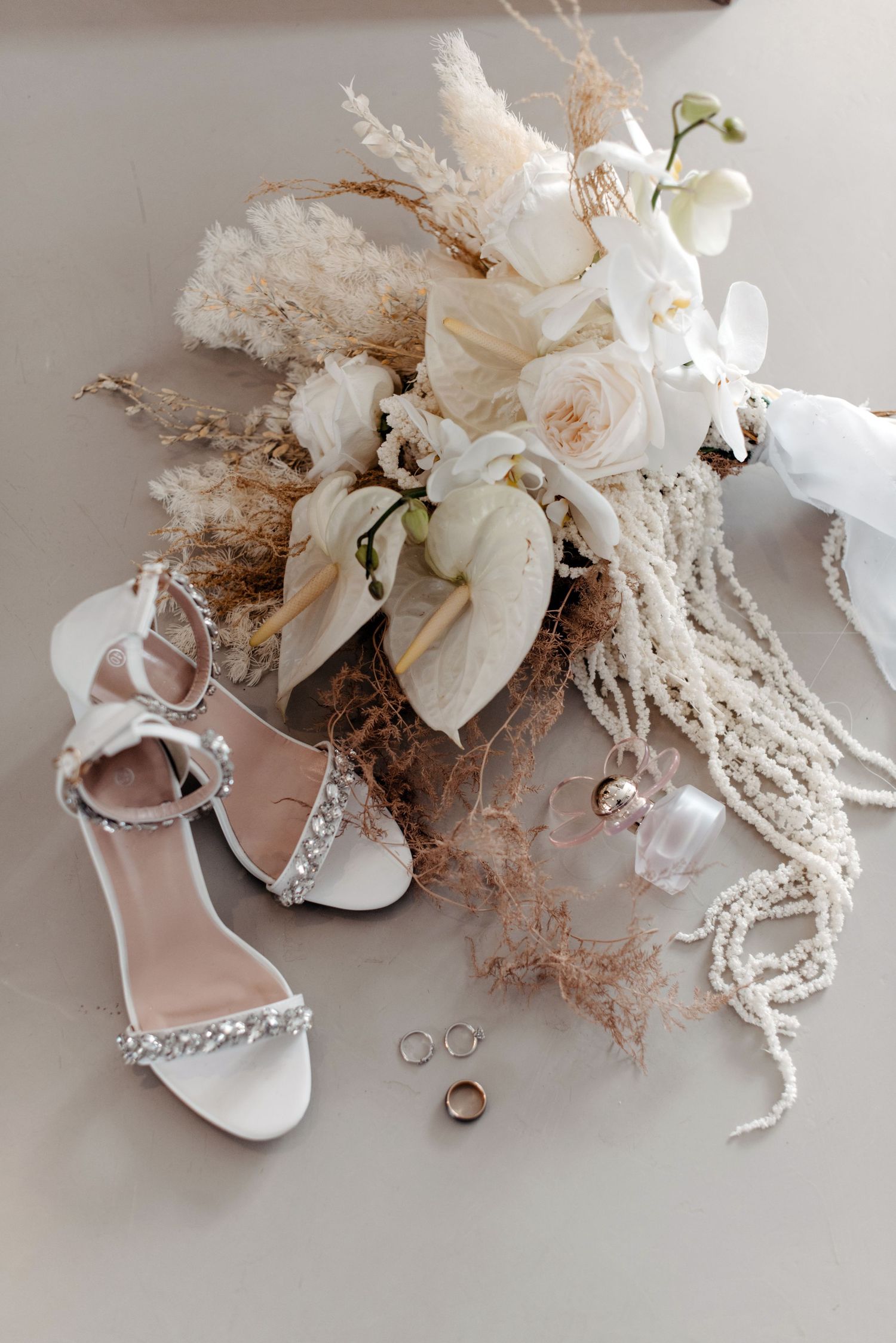 Wedding accessories including white shoes, delicate lace, floral decorations and rings arranged artistically on a light surface.
