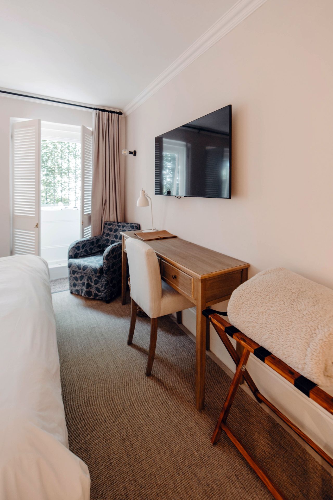 Modern hotel room interior with wall-mounted TV, wooden desk, and carpeted floor showing multiple angles of the space.