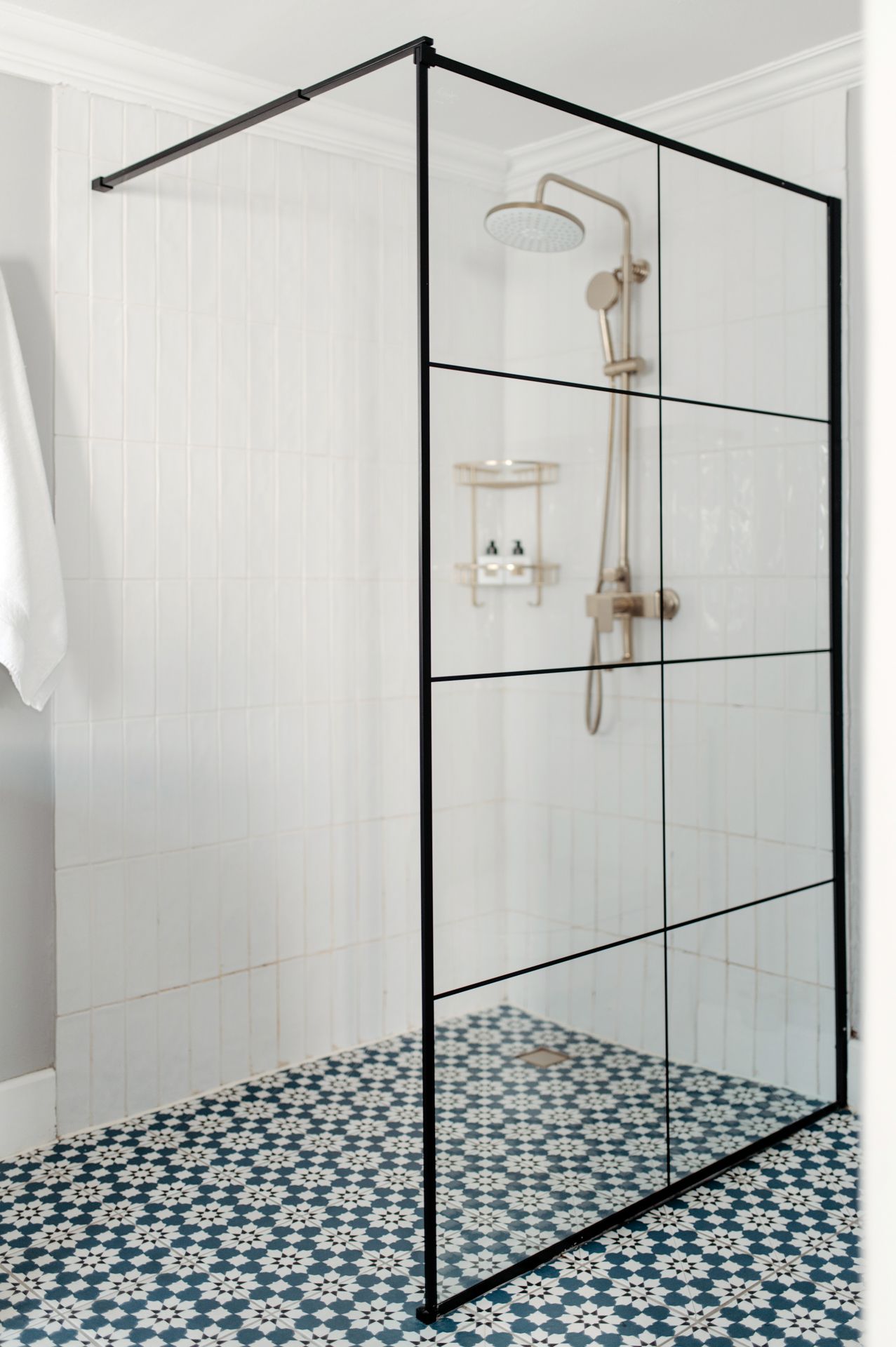 Modern bathroom features black-framed glass shower enclosure and geometric blue and white patterned floor tiles.