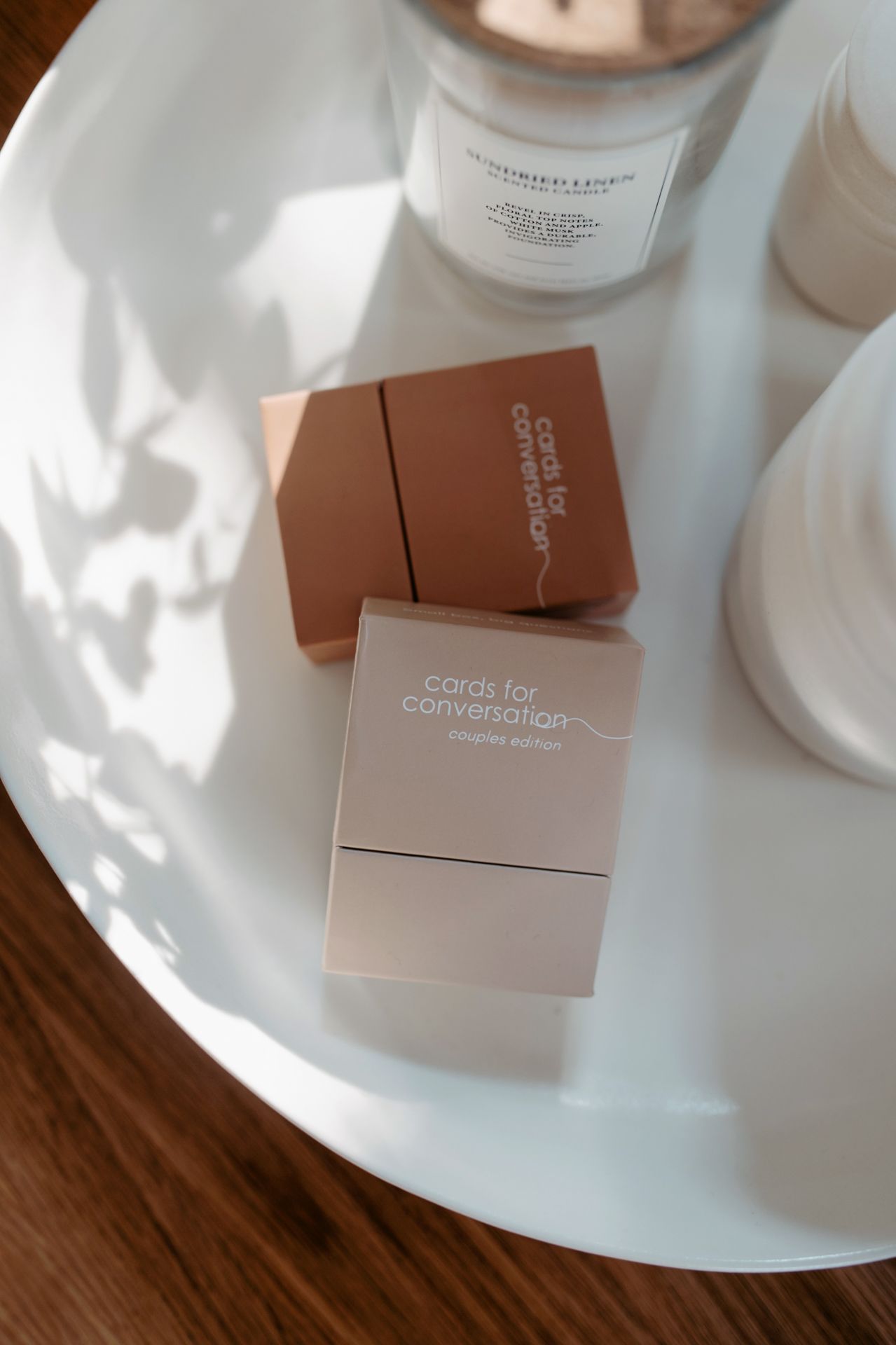 Conversation cards and skincare products arranged on white plates against a wooden surface in warm lighting.