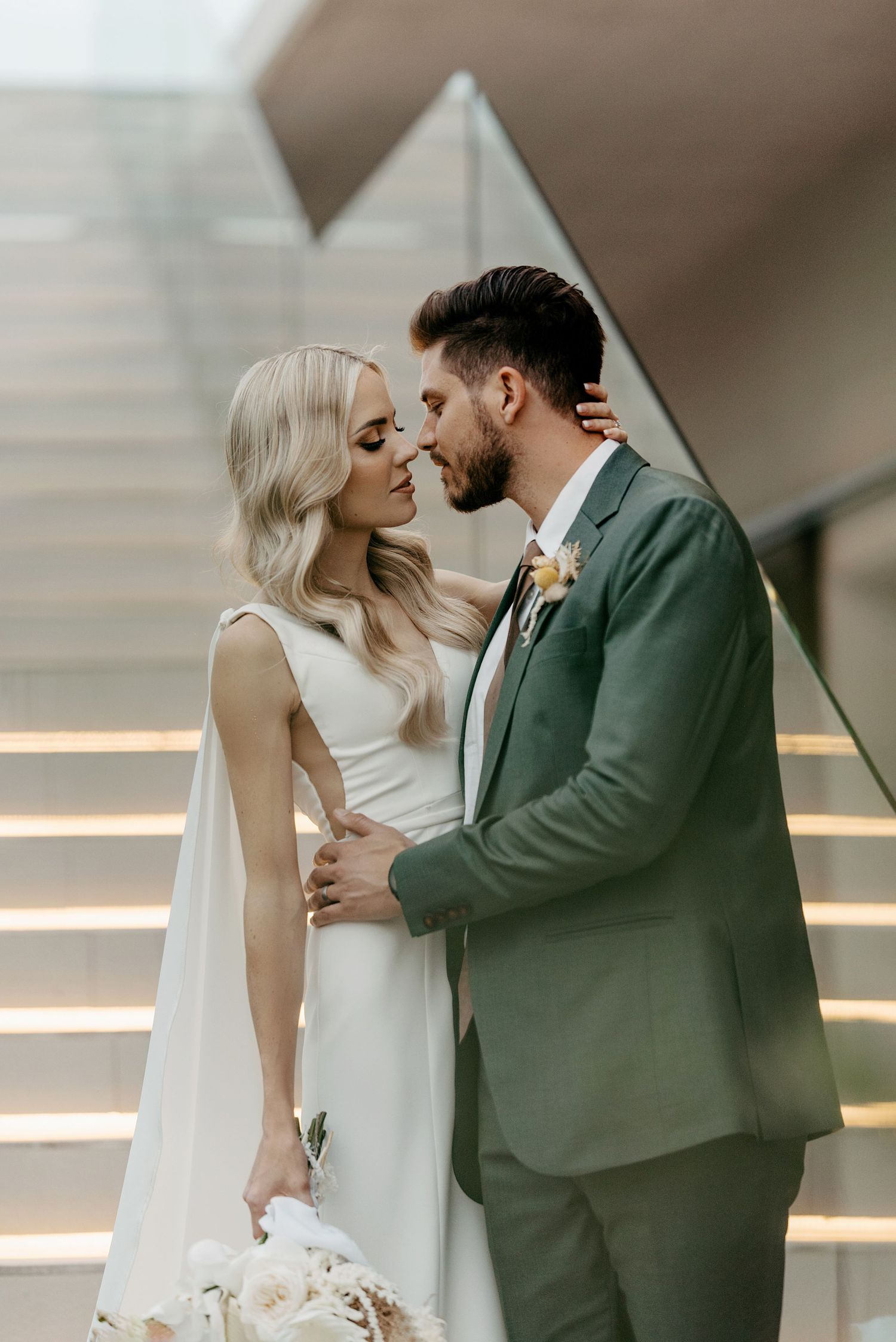 Stylish wedding couple sharing romantic moment on modern staircase.