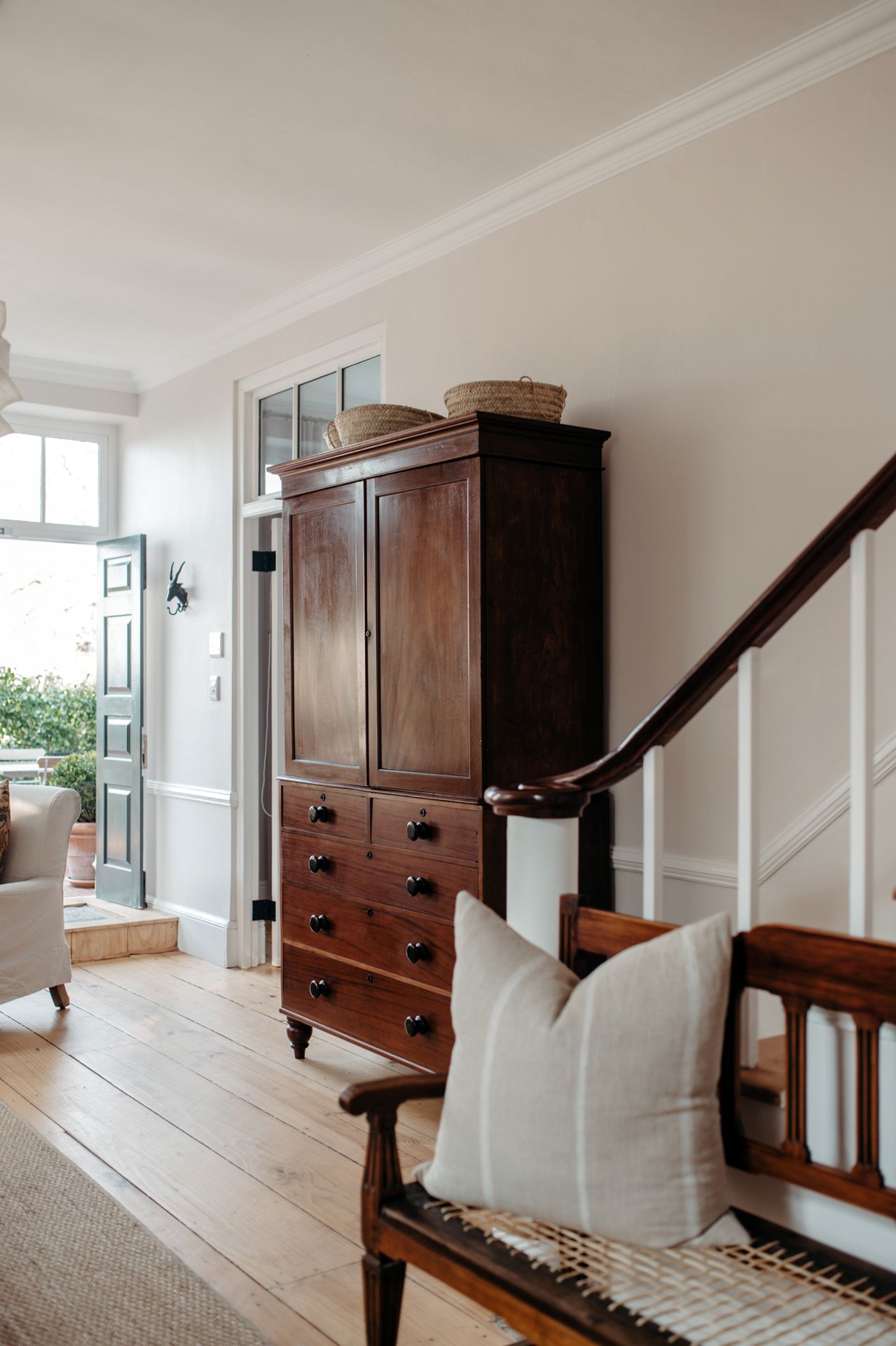 Antique wooden armoire and bench in a bright entryway with hardwood floors and white walls.