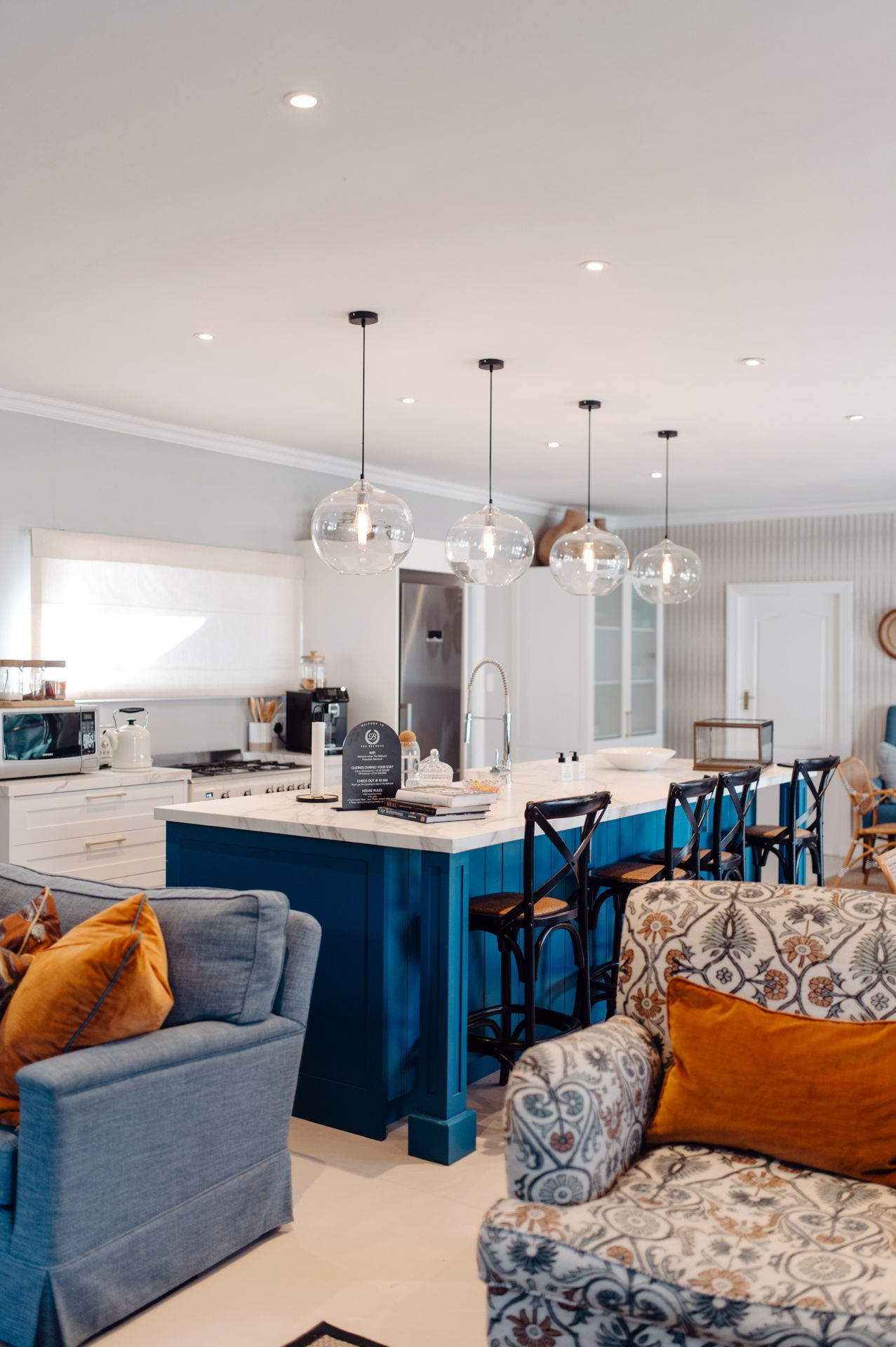 Modern kitchen with navy blue island, glass pendant lights, and cozy seating area featuring orange accent pillows.