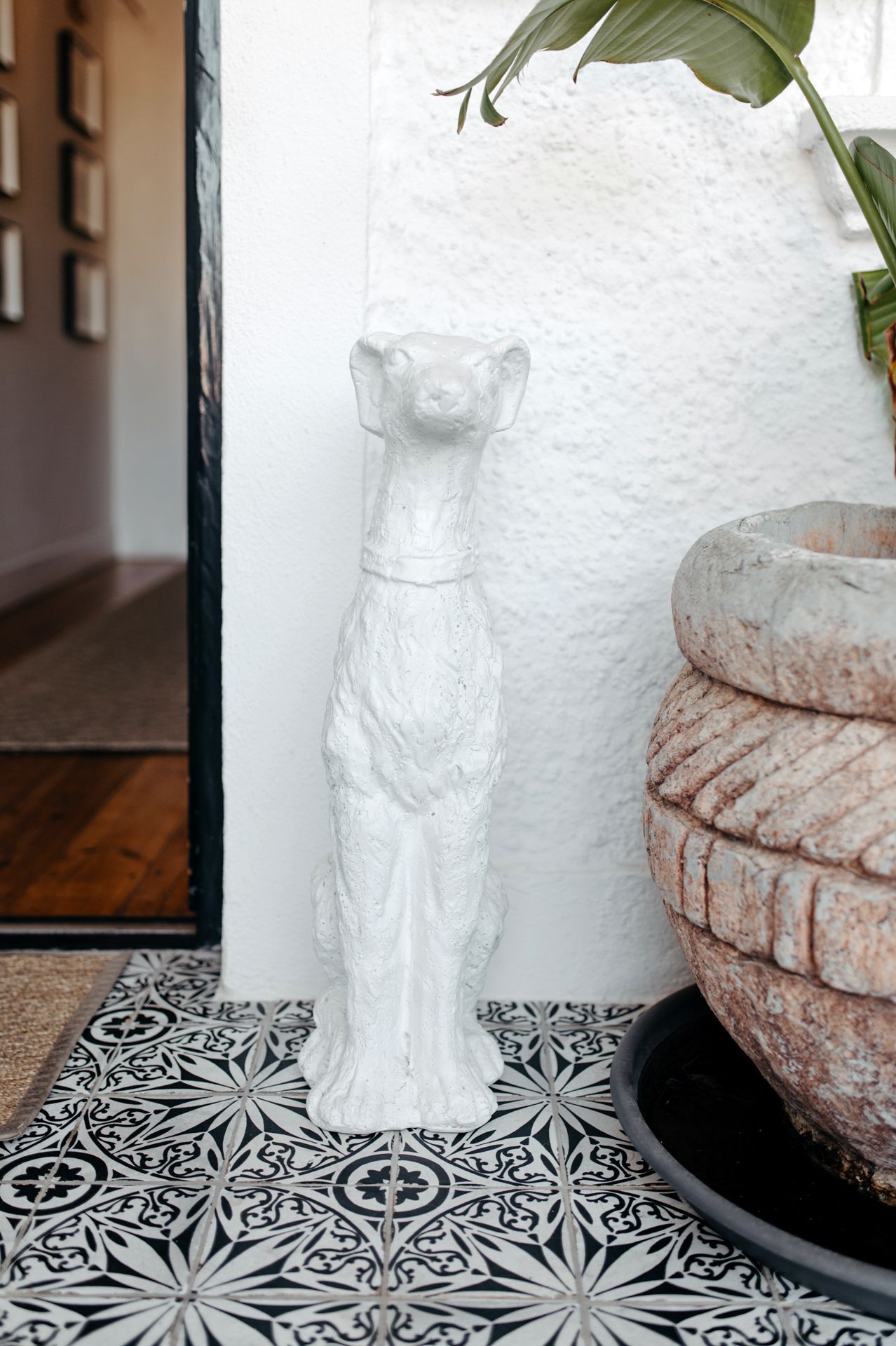White ceramic cat figurine displayed on black and white patterned tile surface next to a decorative clay pot.
