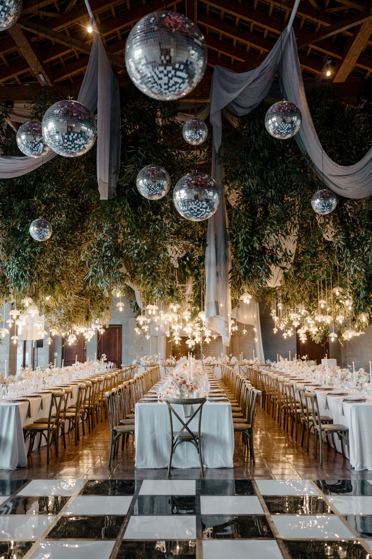 Elegant reception hall decorated with disco balls, draped fabric and hanging lights.