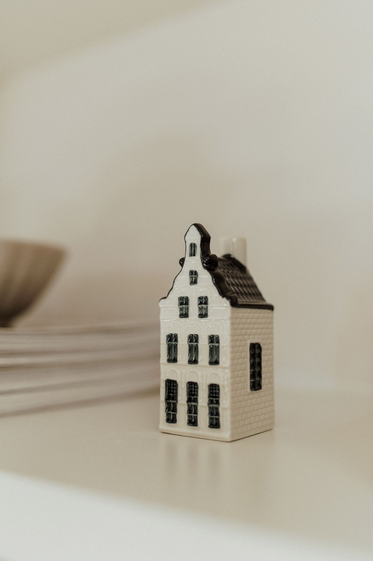 A miniature white ceramic Dutch house decoration with black windows and stepped gable roof on a light surface.