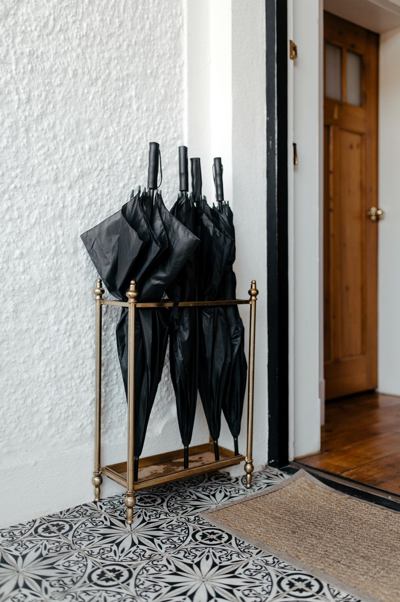 Modern umbrella stand with black umbrellas displayed on a geometric tiled floor in an entryway.