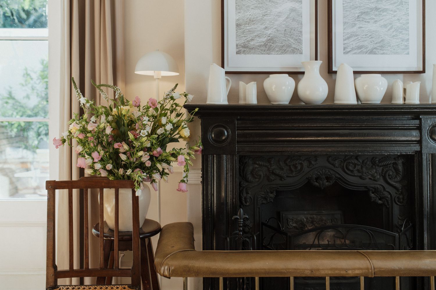 Cozy living room interior with natural light, white walls, dark fireplace, and floral arrangement on wooden table.