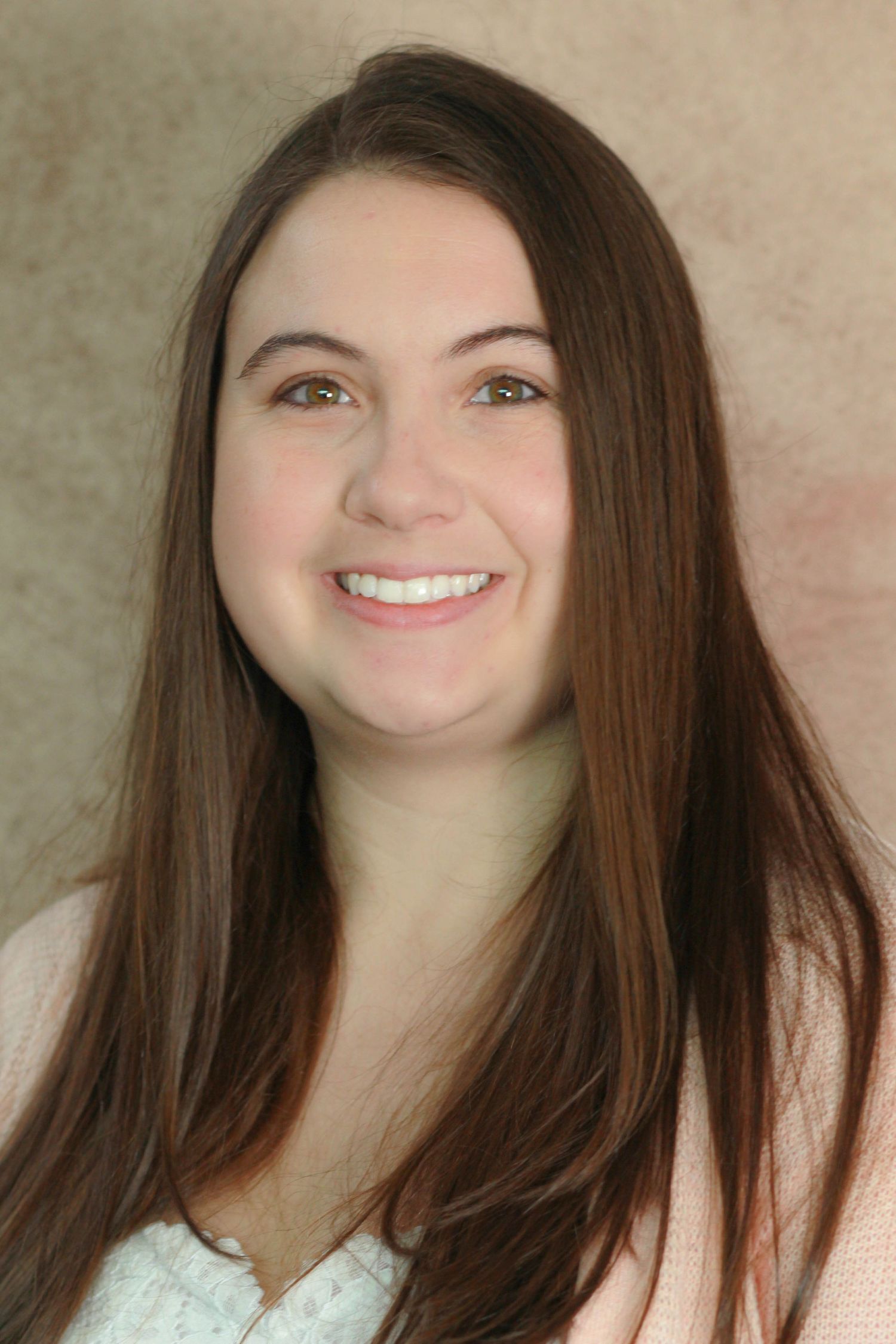 Professional headshot of person with long dark hair and bright smile against neutral background.