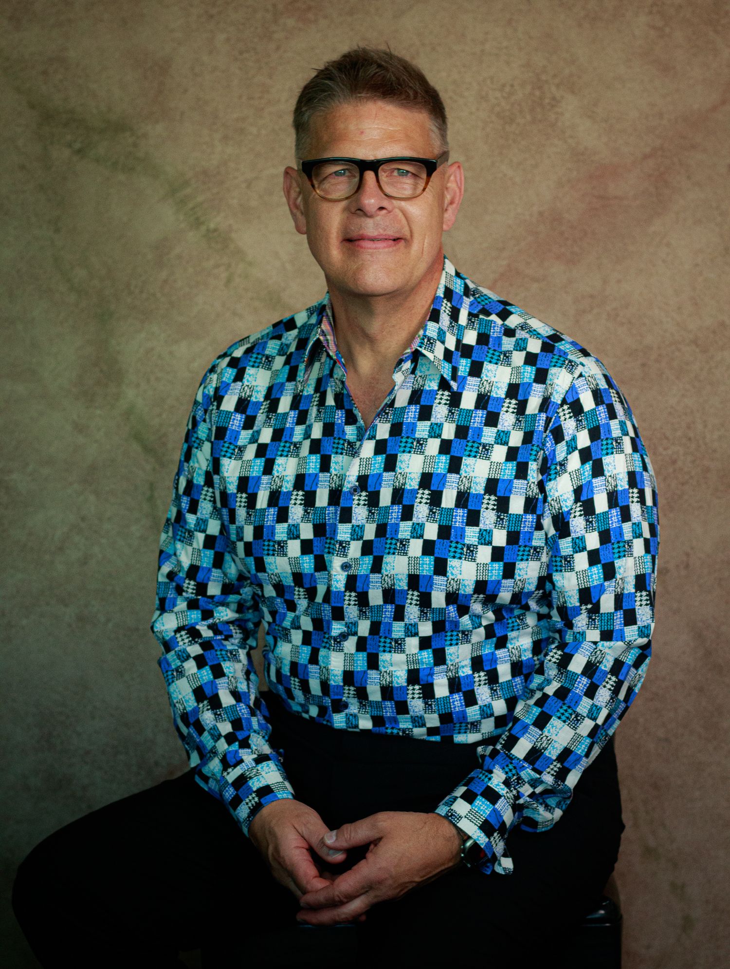 Studio portraits featuring someone wearing a vibrant blue checkered pattern shirt against a textured brown backdrop.