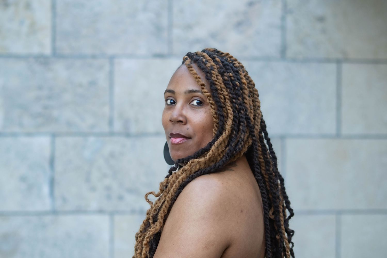 A person with braided hair poses against a gray brick wall in a series of expressive portraits.